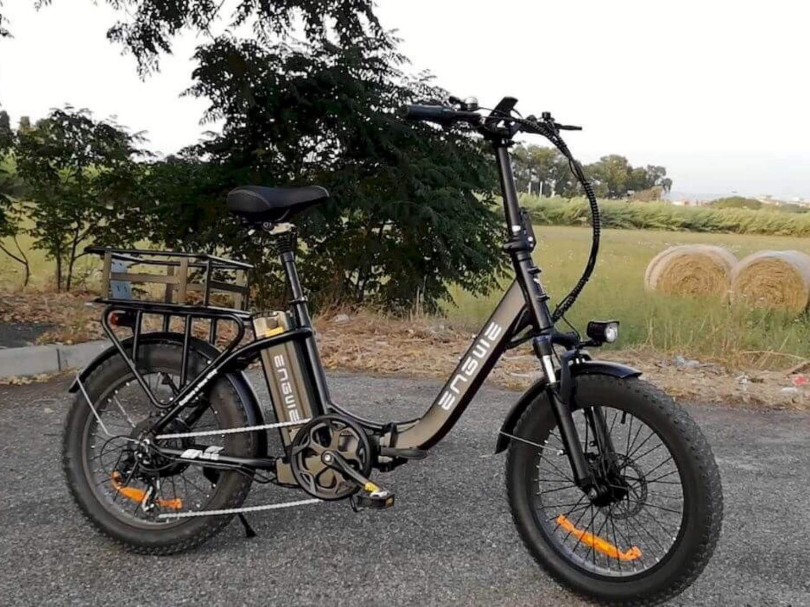 Bicicletta elettrica nera su strada con balle di fieno. Alberi verdi e cielo blu sullo sfondo.