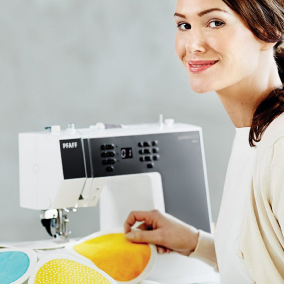 Una mujer sonriendo mientras cose en una máquina de coser Pfaff blanca. Patrones en la mesa.