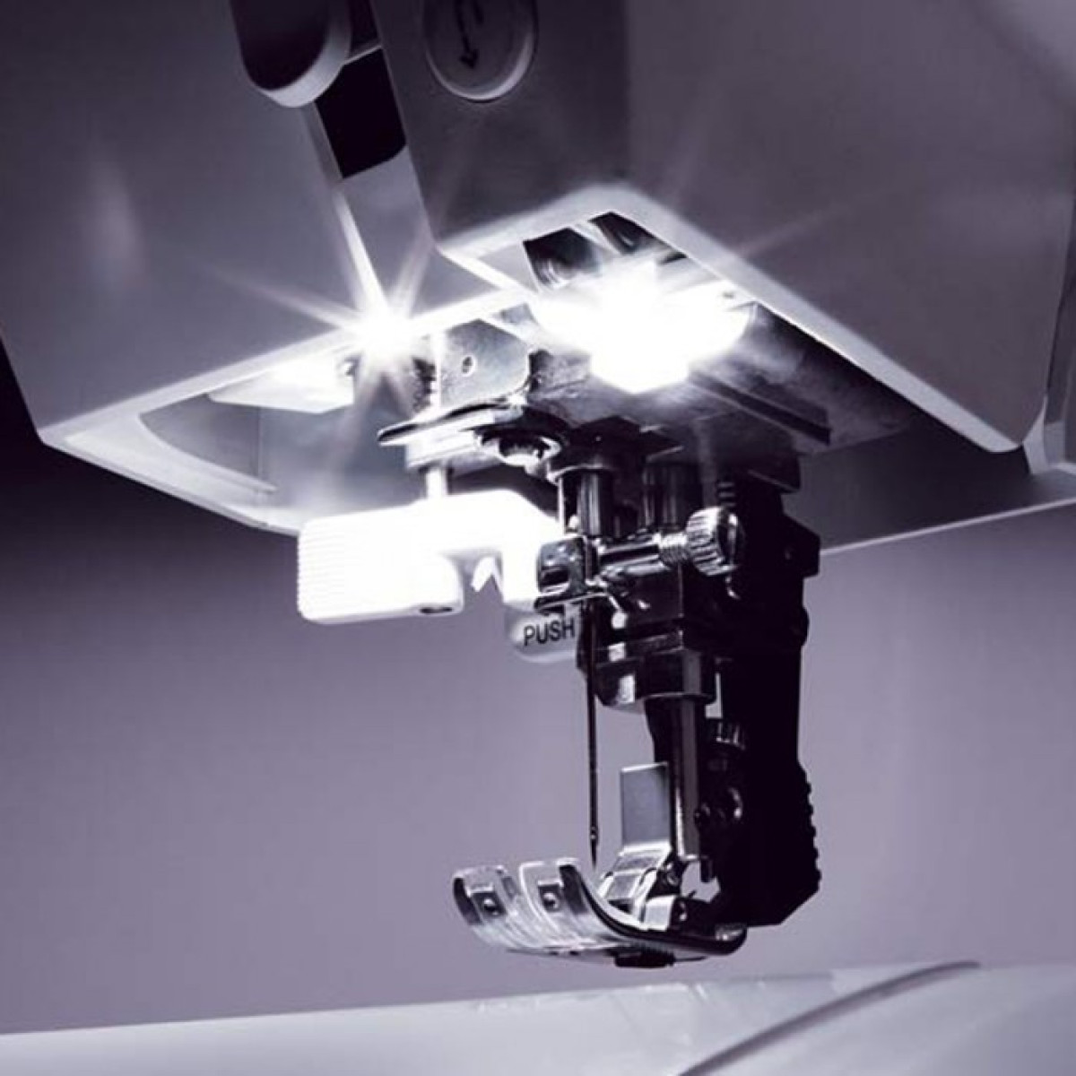 Primer plano de aguja y prensatelas de una máquina de coser, con luz brillando.