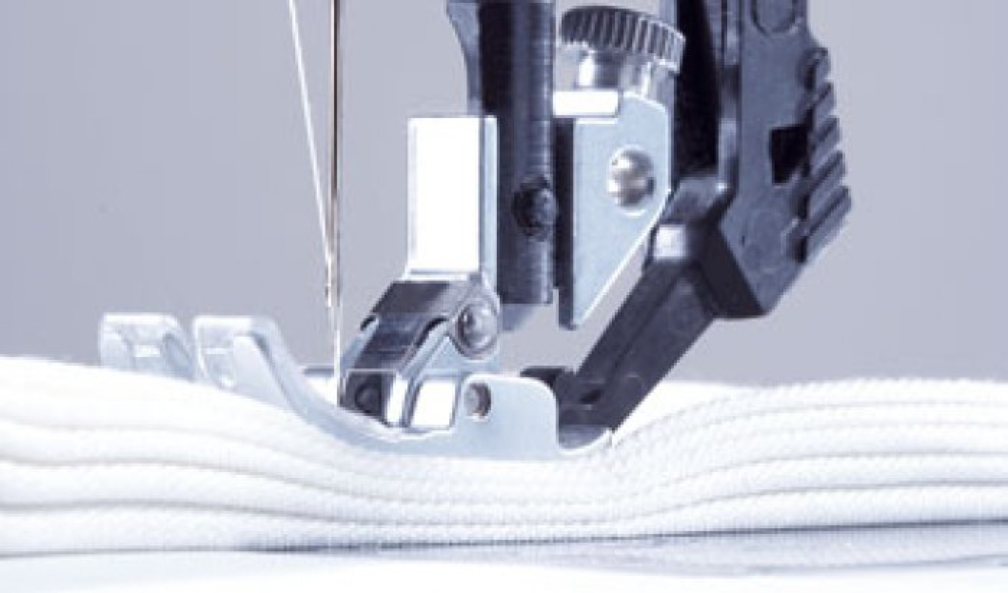 Primer plano del prensatelas de una máquina de coser presionando sobre tela blanca con aguja visible.