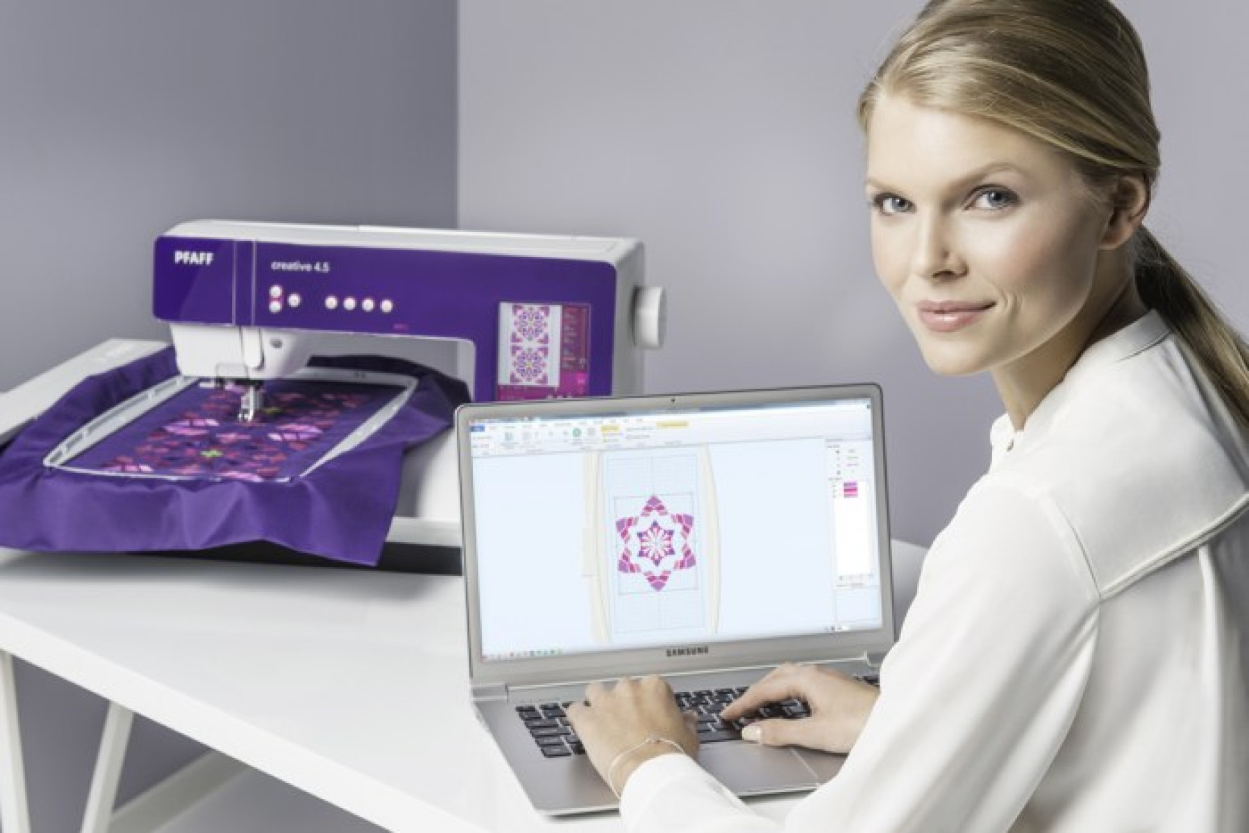 Mujer usando una laptop con una máquina de coser en el fondo. La máquina es morada y blanca.