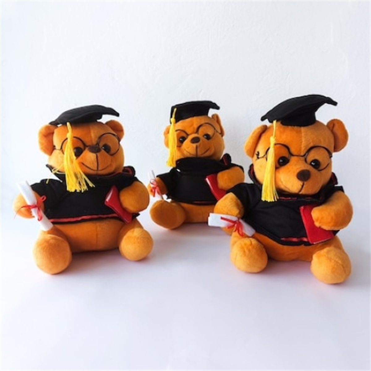 Drei Teddybären-Absolventen mit Mützen, Roben, Brillen, halten Diplome, weißer Hintergrund.