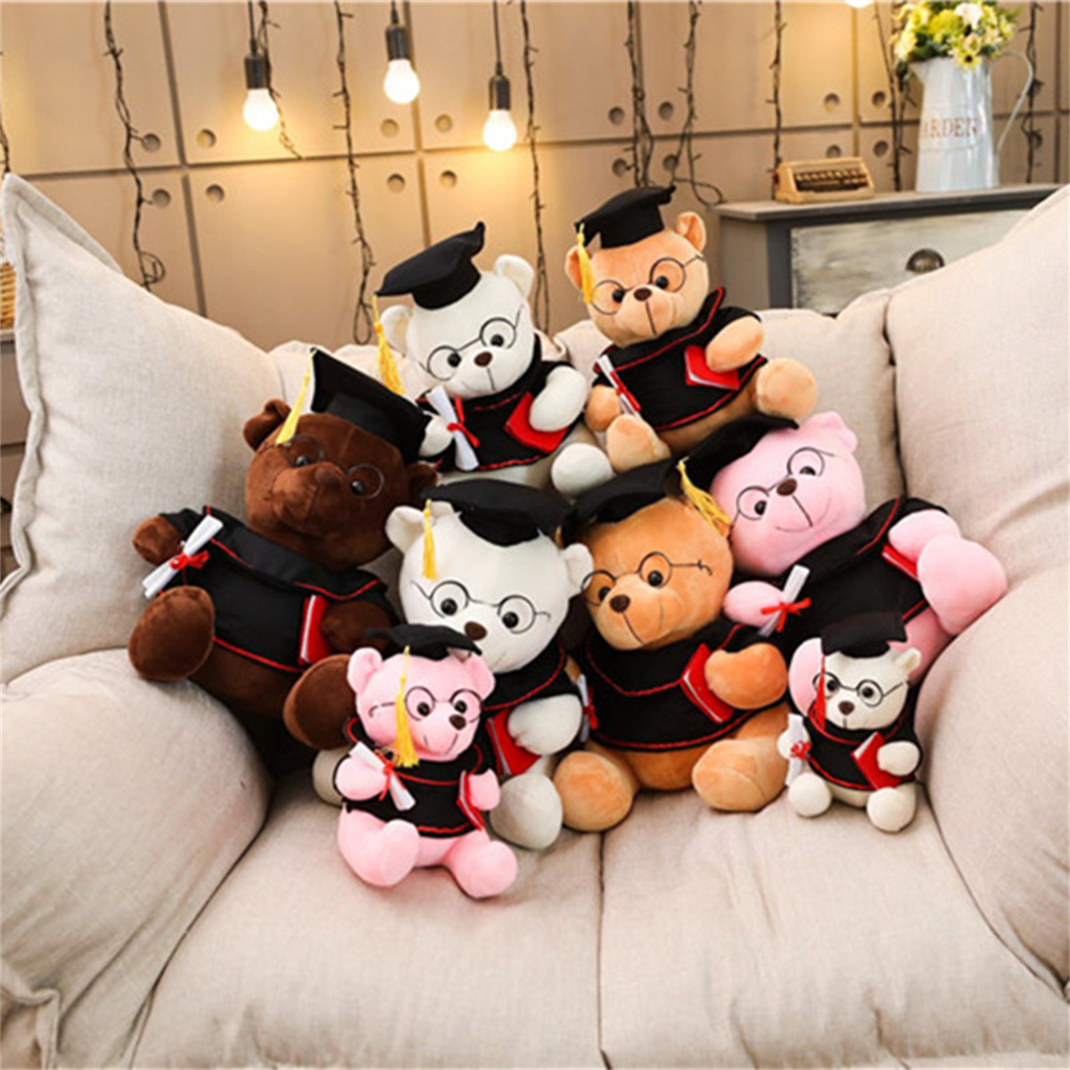 Abschluss-Teddybären auf einer Couch. Sie tragen schwarze Roben und Kappen mit Diplomen. Hintergrund: eine Zierwand.