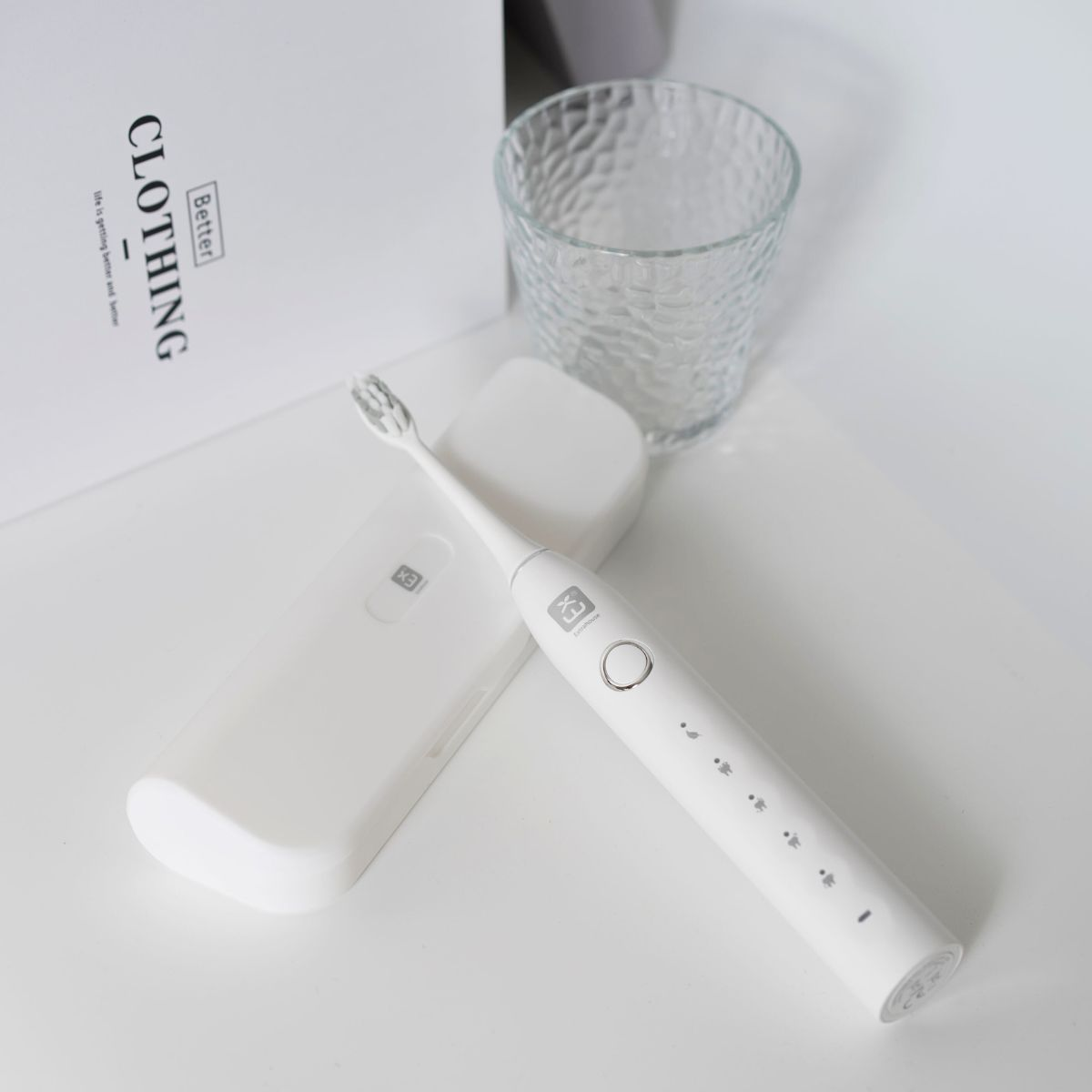 Cepillo de dientes blanco, estuche y vaso sobre superficie blanca.