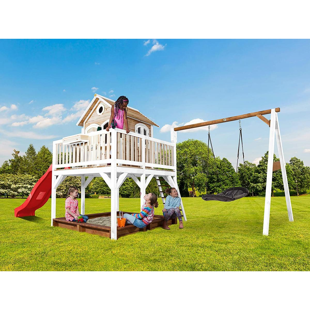 Kinder spielen auf einem Spielplatz aus Holz. Rutsche, Schaukeln und Sandkasten auf Rasenfläche.