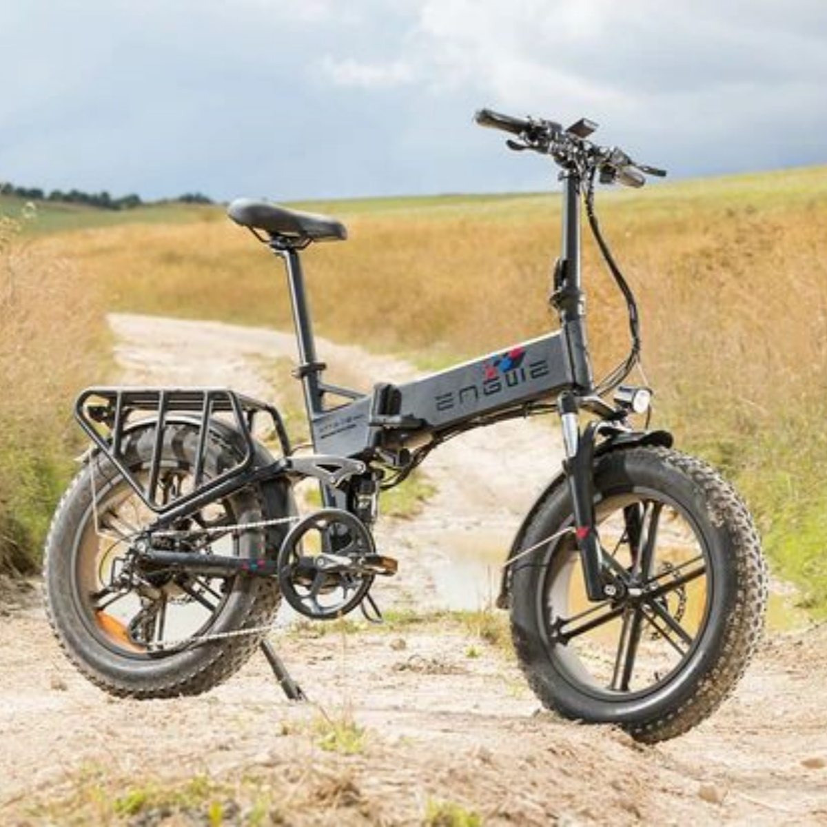 Bicicletta elettrica nera e grigia su strada sterrata, con erba alta sullo sfondo, giornata di sole.