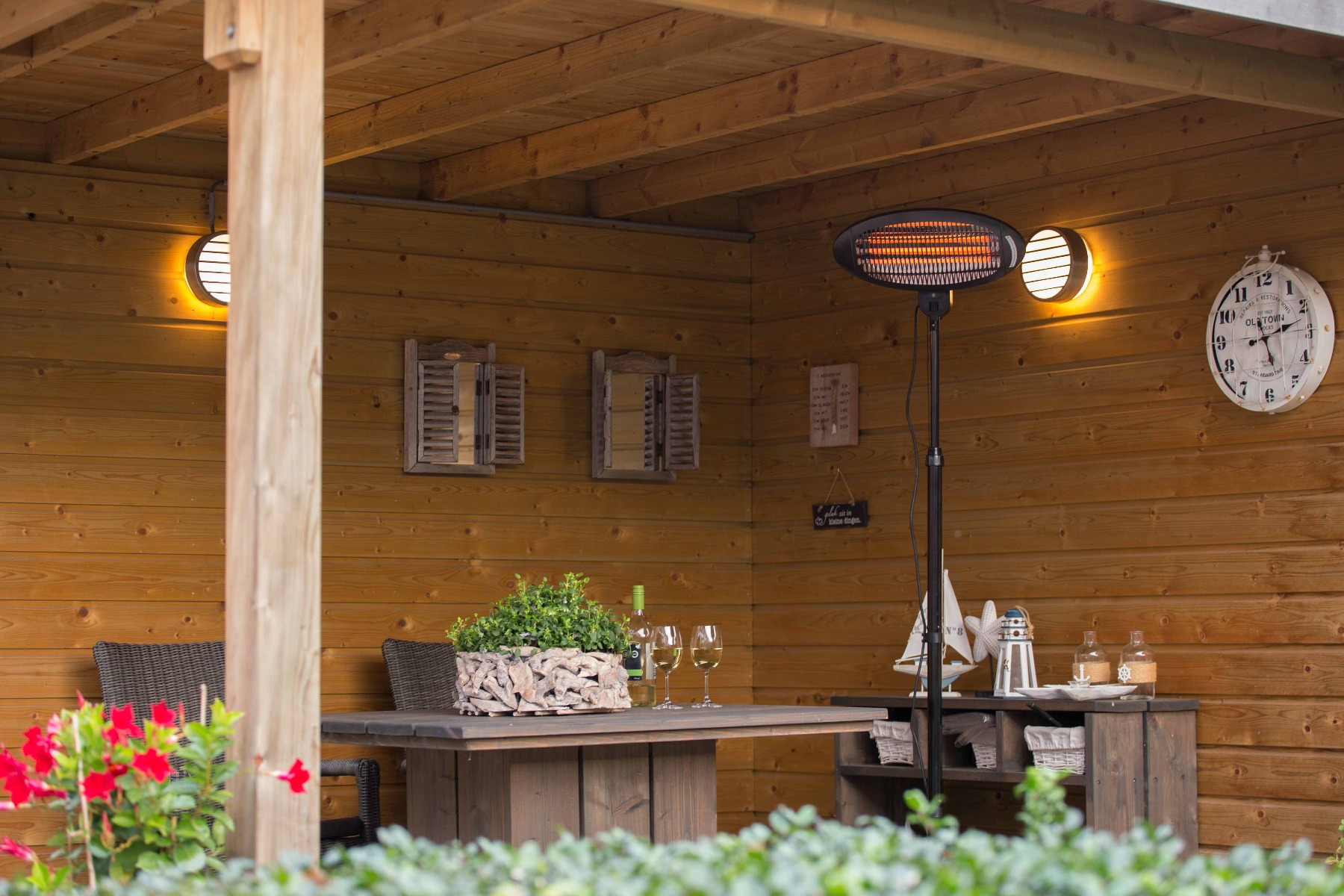 Holzterrasse mit Tisch, Heizung und Dekorationen, beleuchtet von zwei runden Lichtern.