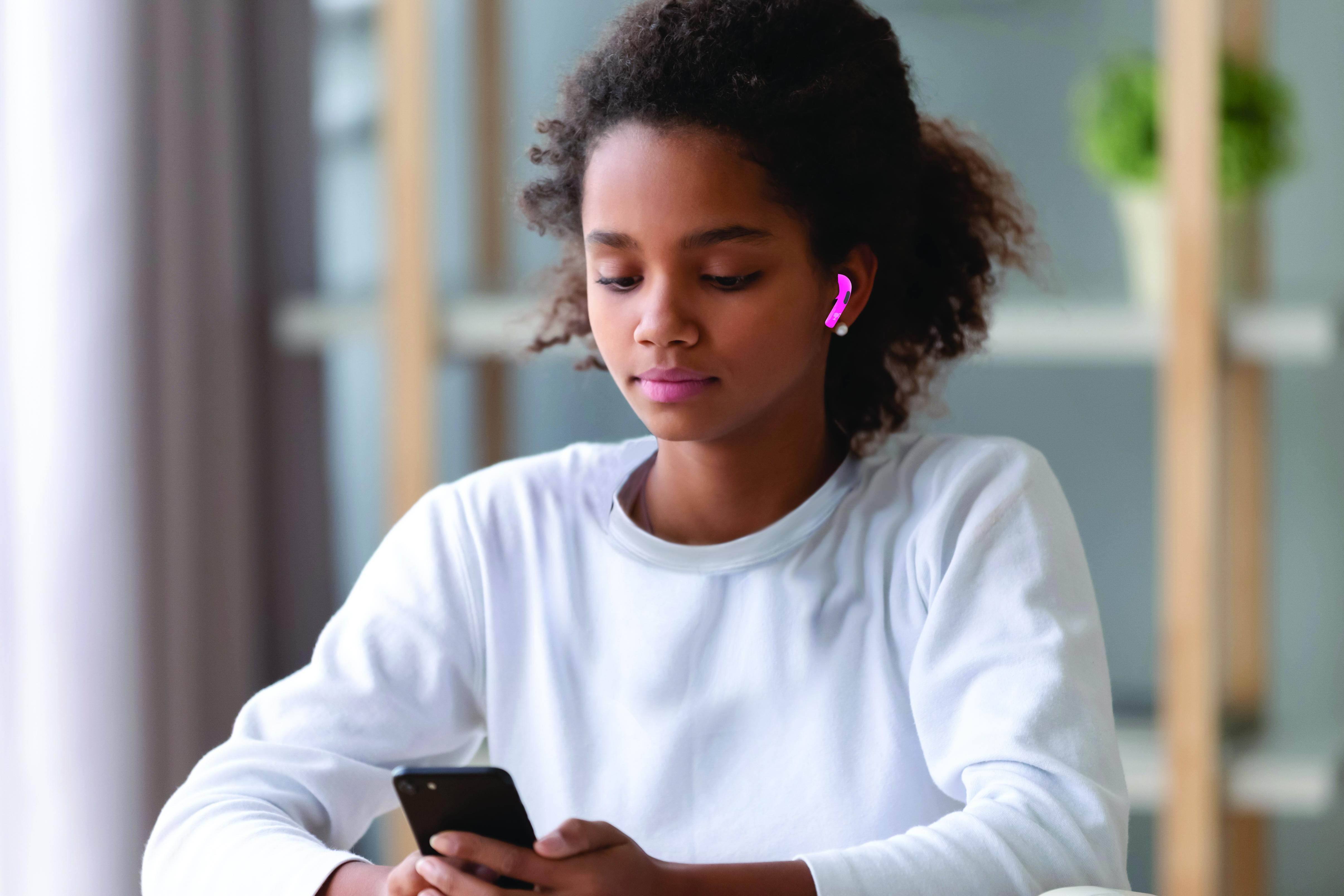 Una joven con auriculares, mirando su teléfono. El fondo está borroso.