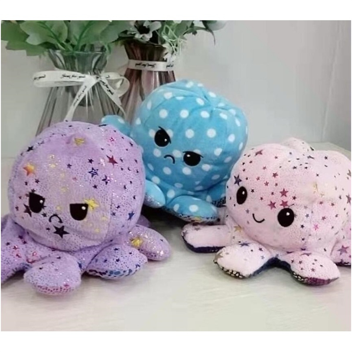 Drei Plüsch-Oktopusse: lila mit Sternen, blau mit weißen Punkten und rosa mit Sternen, auf weißer Oberfläche.