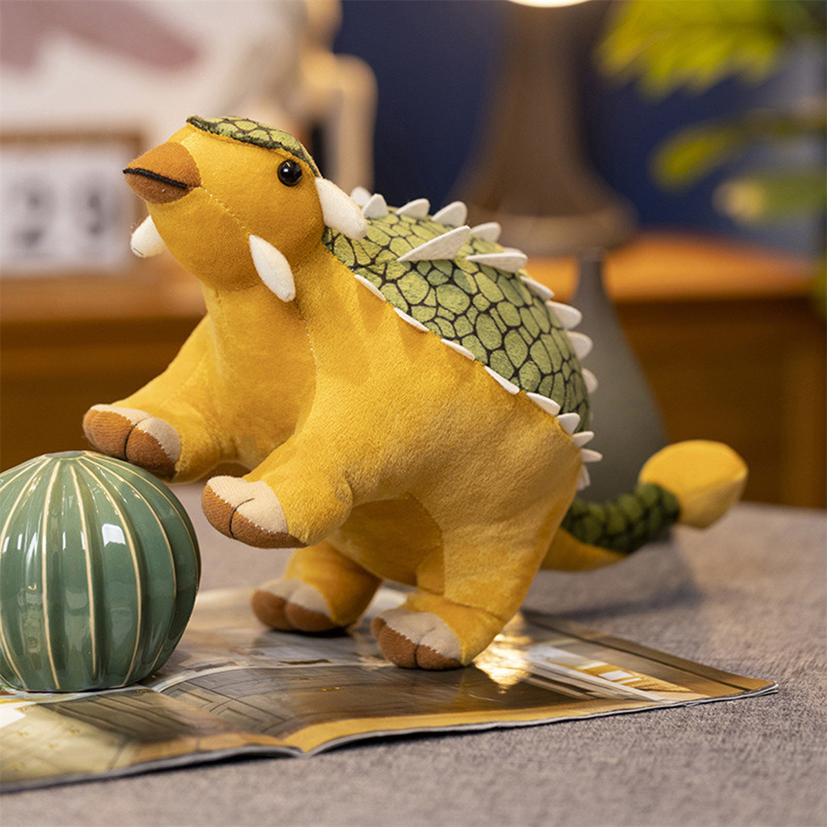 Gelbes Dinosaurierspielzeug mit grünen Stacheln und einer grünen Kugel daneben.