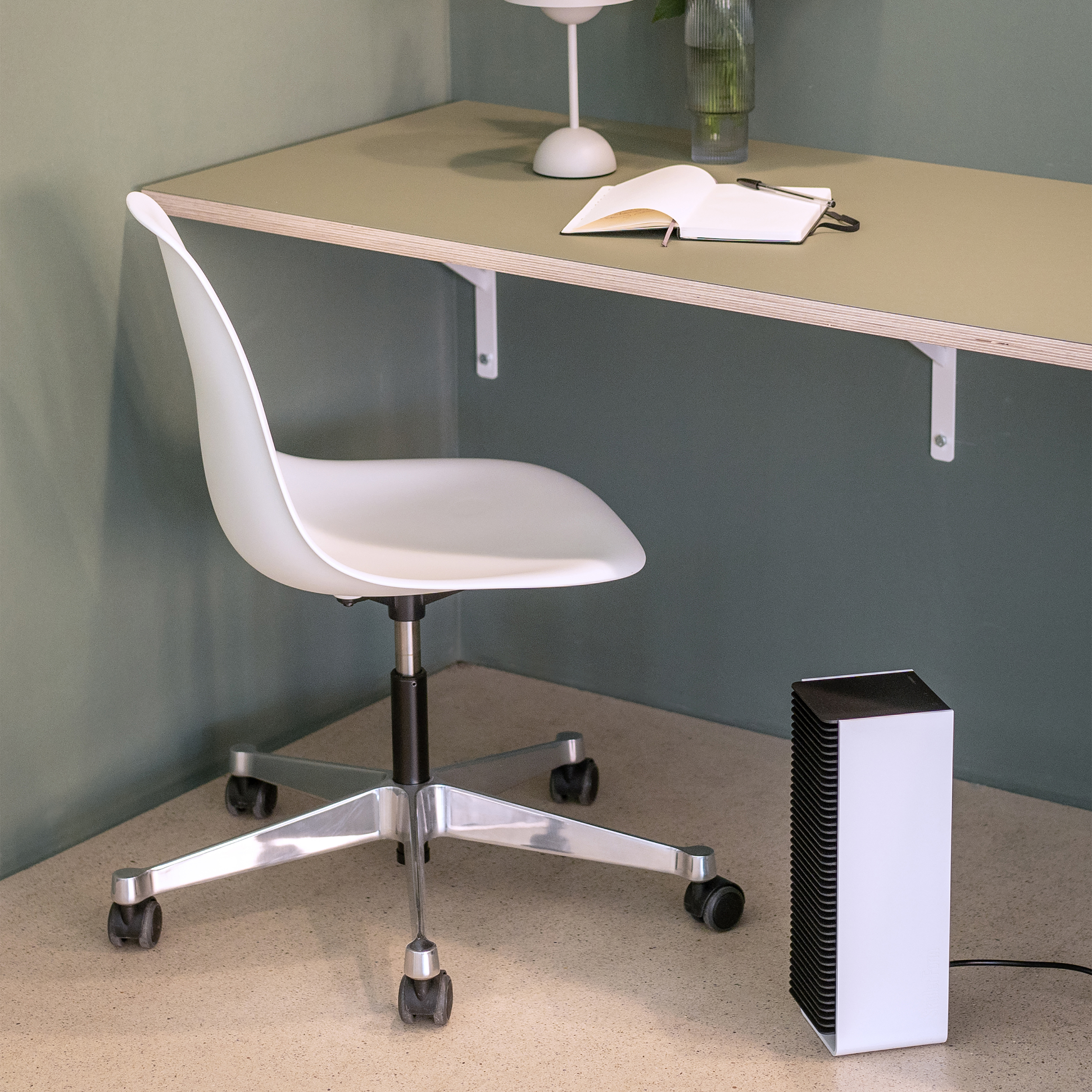 Een witte stoel, een bureau en een zwarte kachel in een kamer met groene muren en een beige vloer.