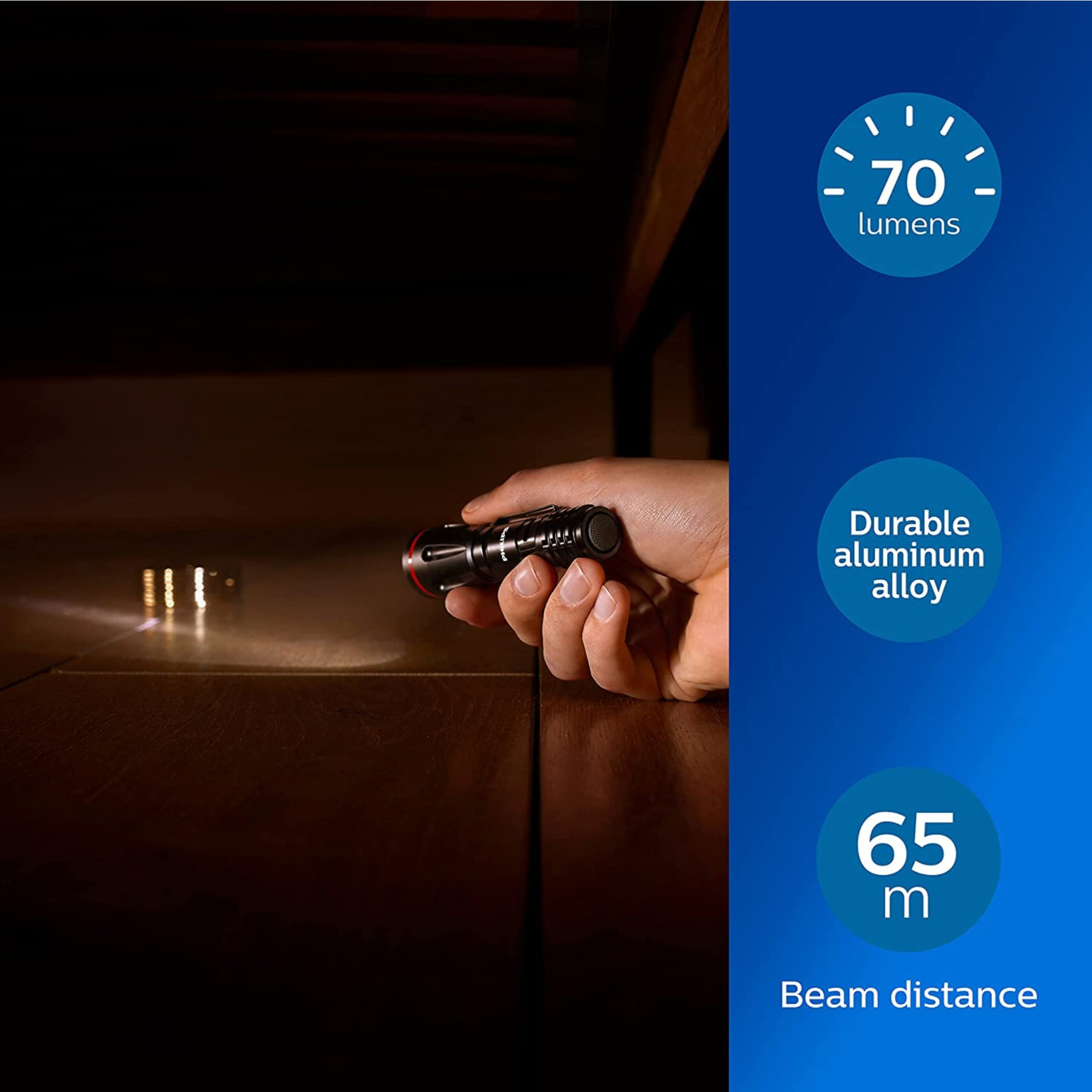 Hand hält eine schwarze Taschenlampe. Lichtstrahl auf brauner Oberfläche. Text: 70 Lumen, 65 m Reichweite.