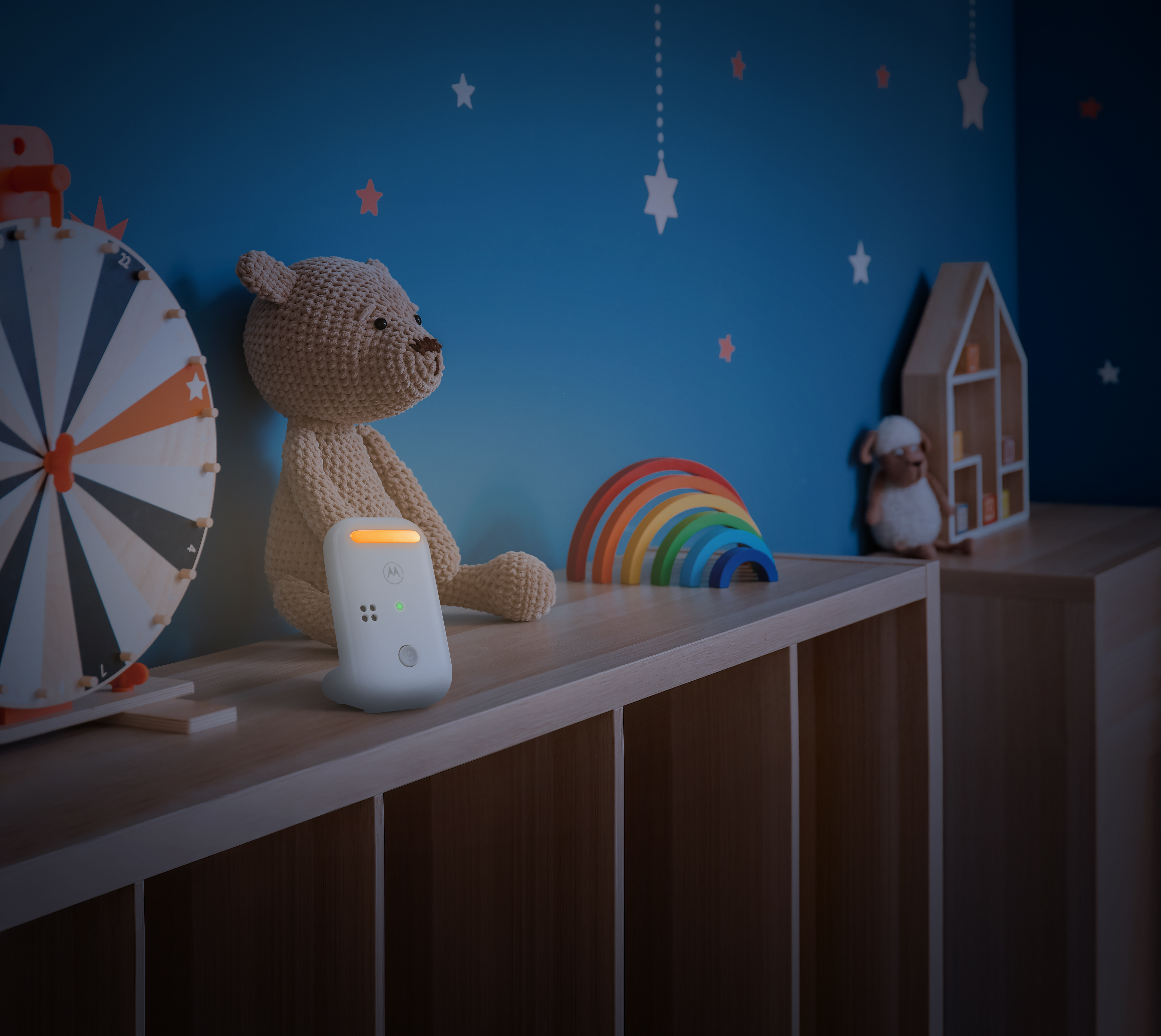 Ein Babyphone mit Spielzeug und einem Regenbogen auf einem Regal im Kinderzimmer.
