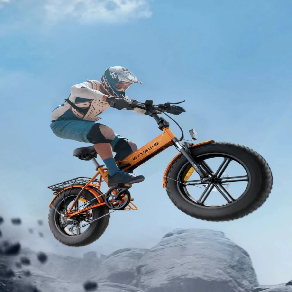 Persona in sella a bici elettrica arancione, salta rocce su sfondo cielo blu.