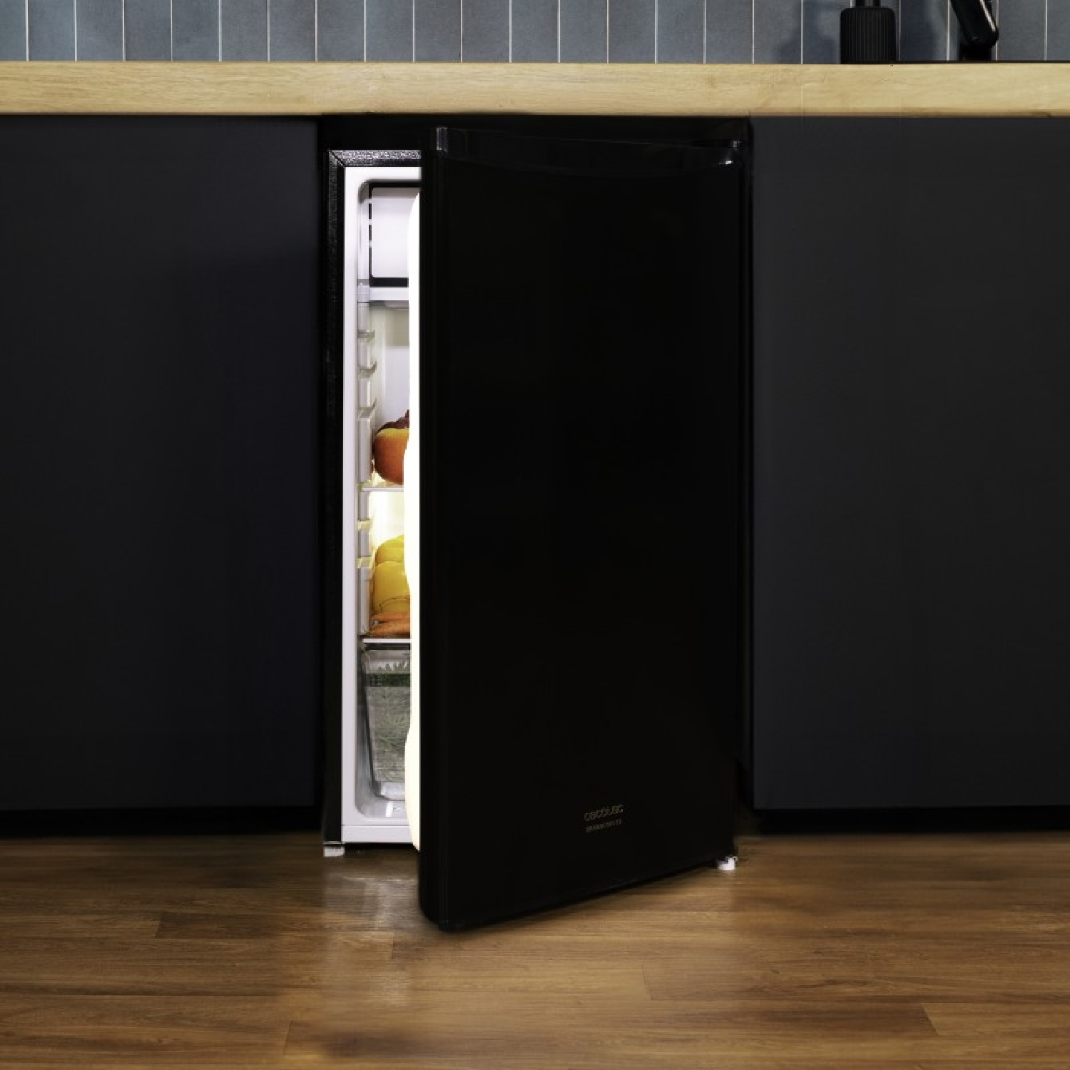 Frigorifero nero con la porta aperta. All'interno ci sono alimenti. Il frigorifero è in una stanza buia.