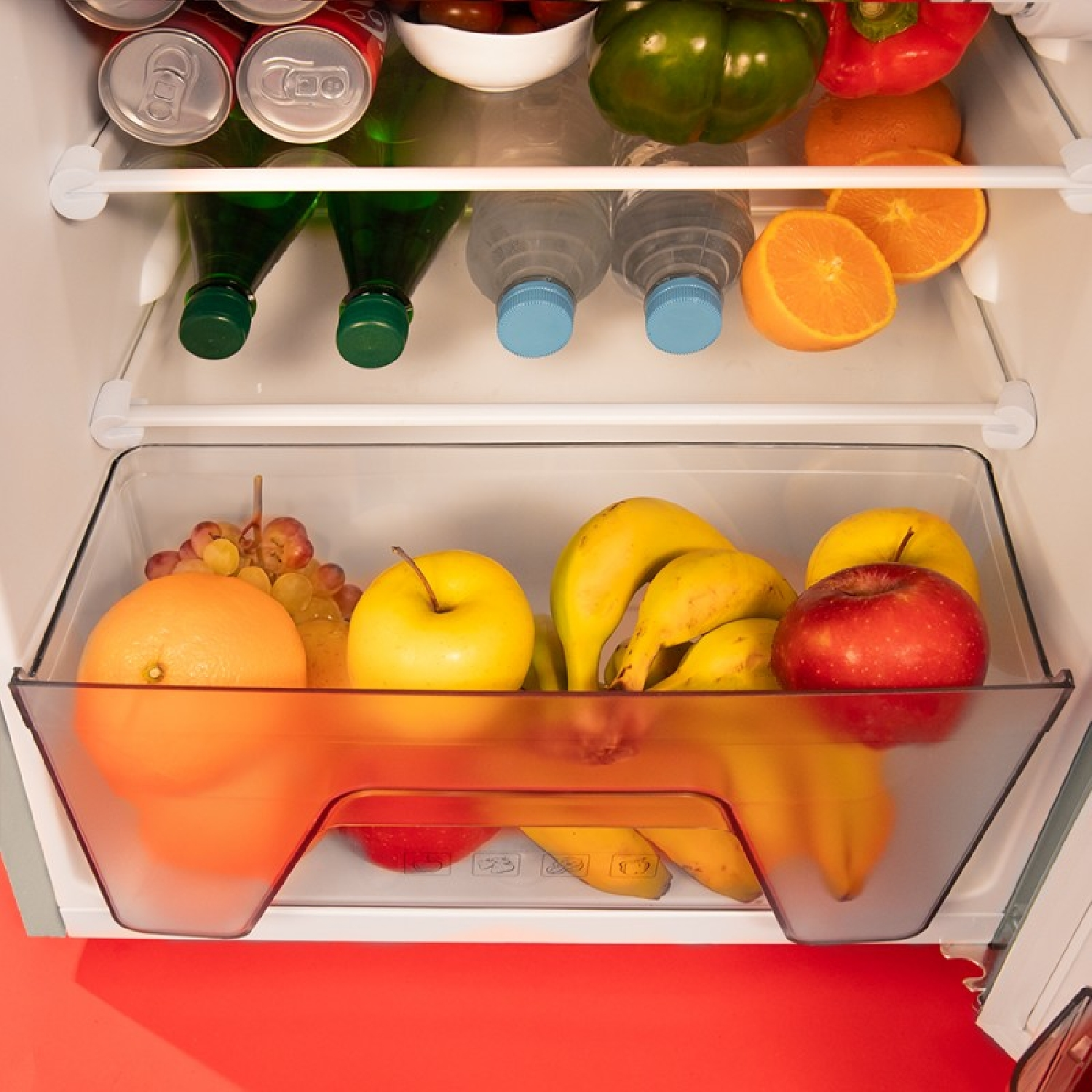 Lodówka z owocami i napojami w szufladach i na półkach. Czerwone wnętrze.