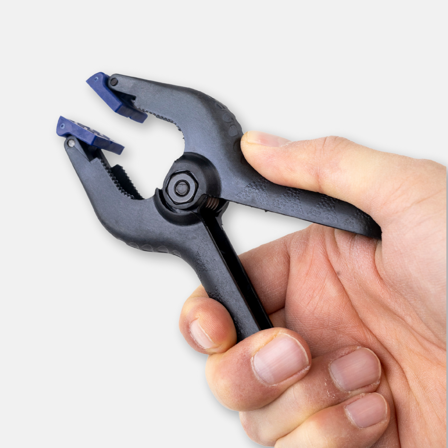 Hand, die eine schwarze Kunststoffklemme mit blauen Gummispitzen hält. Die Klemme ist offen.