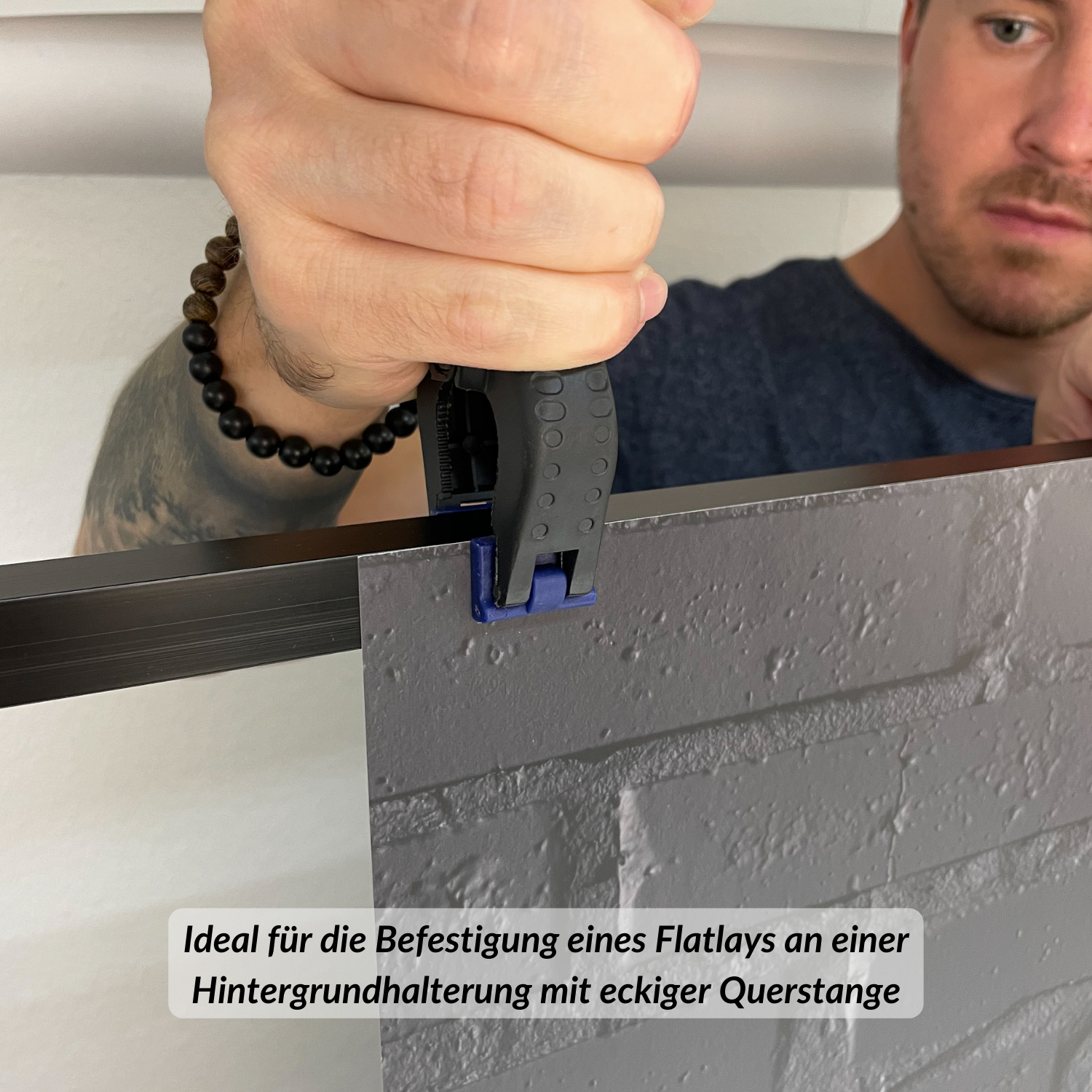 Ein Mann befestigt mit einem Werkzeug eine graue Ziegelplatte an einem schwarzen Metallrahmen.
