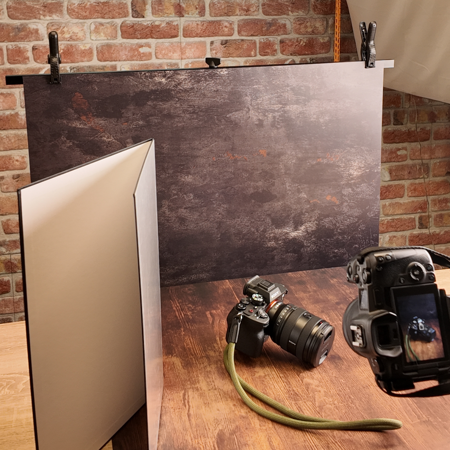 Studio-Setup mit Kameras, Reflektoren und Hintergrund. Ein Holztisch und eine Ziegelmauer sind sichtbar.