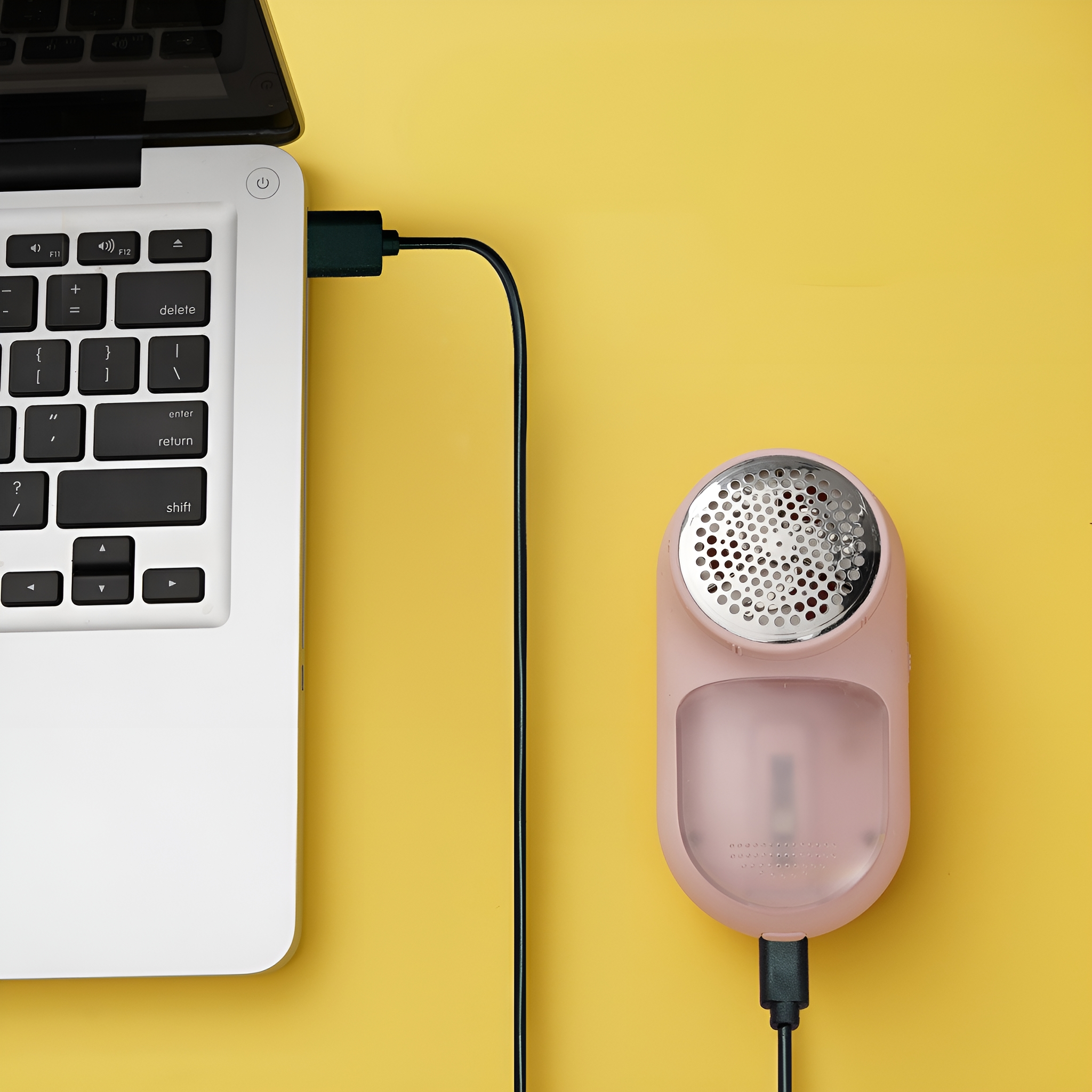 Ein rosa Fusselentferner, der über ein schwarzes USB-Kabel mit einem Laptop verbunden ist, vor gelbem Hintergrund.