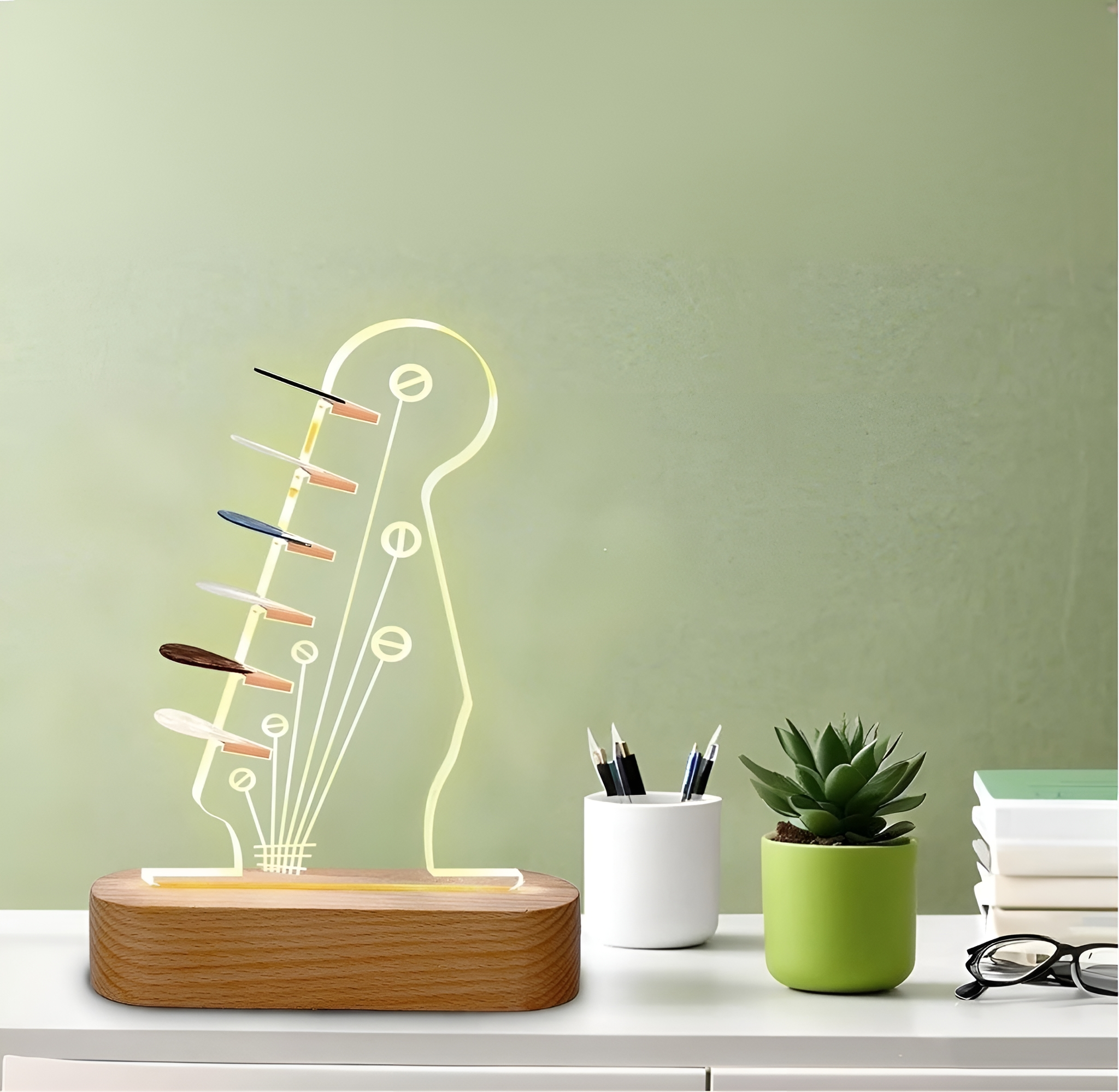 Eine gitarrenförmige Lampe mit Lichtern, eine kleine Sukkulente, Stifte und Bücher auf grünem Hintergrund.