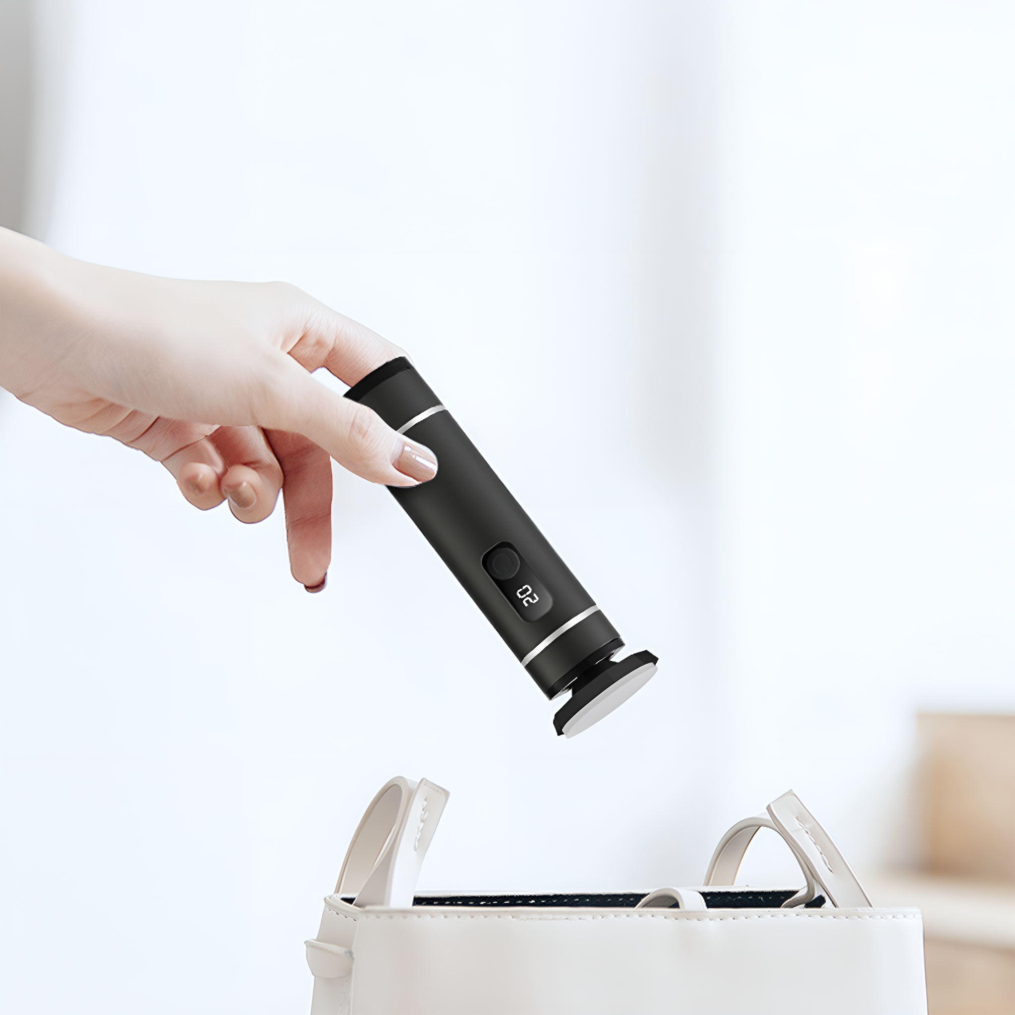 Eine Hand hält ein schwarzes Gerät, möglicherweise einen Weinöffner, über einer weißen Handtasche.