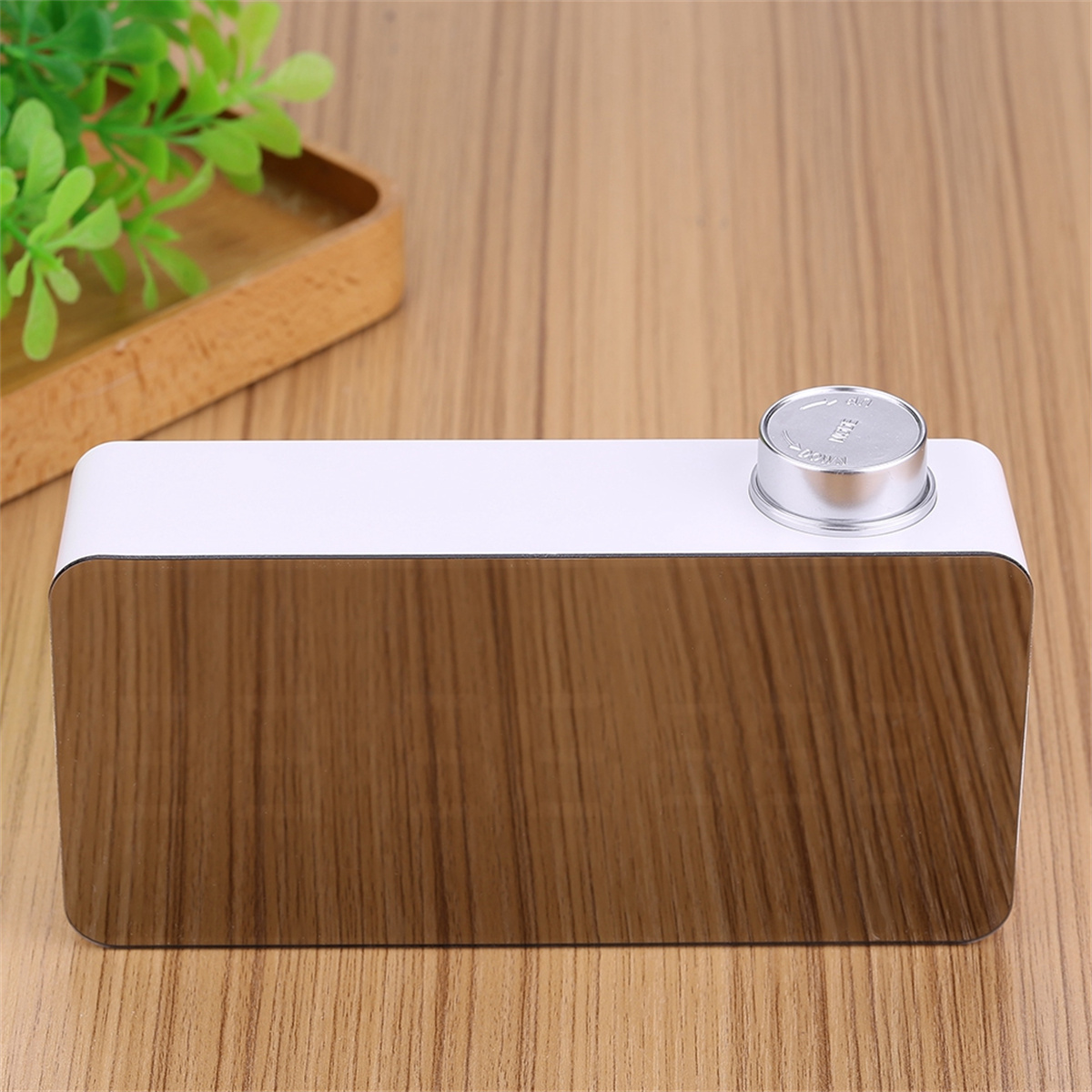 Eine weiße und verspiegelte Digitaluhr. Sie steht auf einer Holzoberfläche mit einem kleinen Holztablett im Hintergrund.
