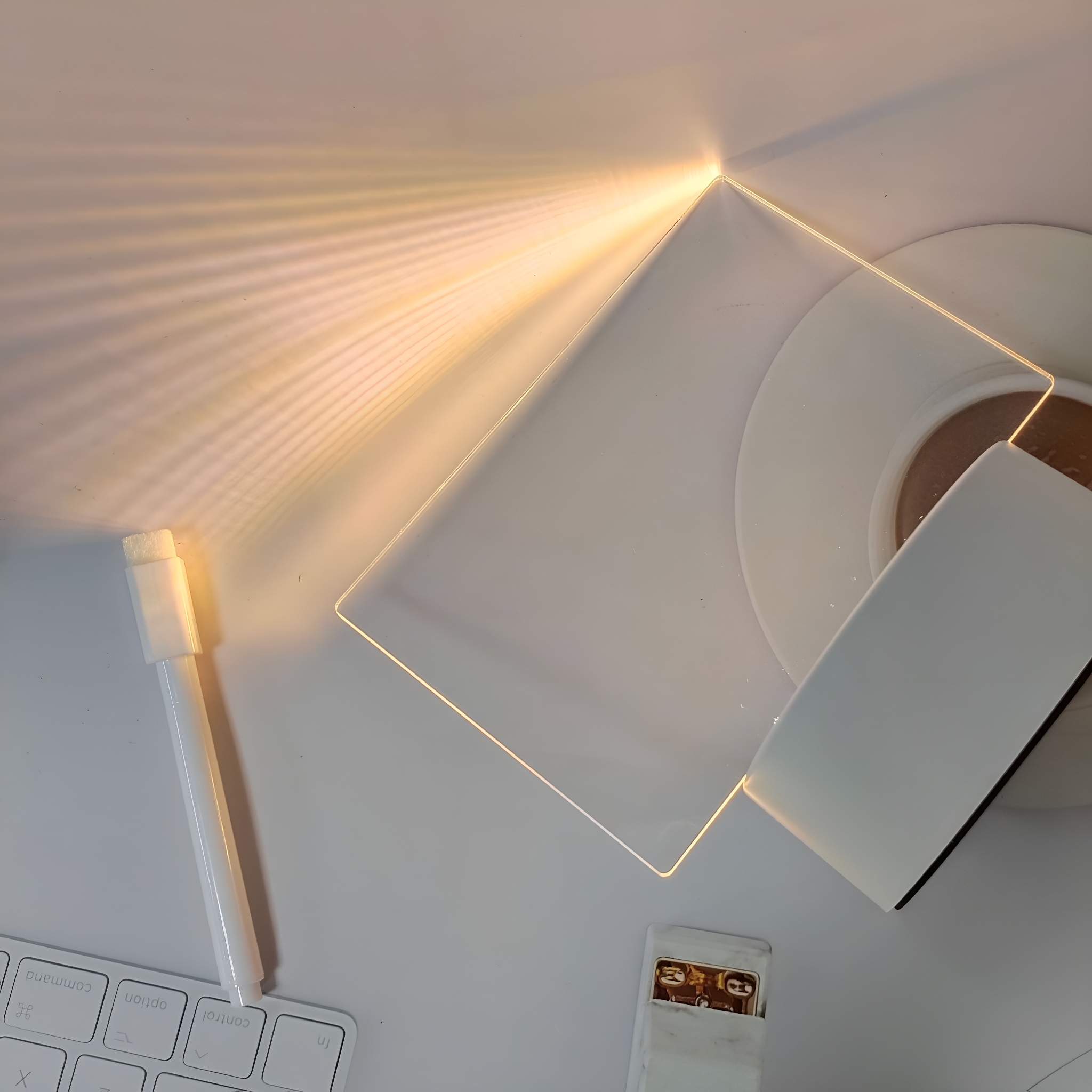 Ein weißer Schreibtisch mit einem Stift, einer Tastatur, einer Lampe und einer weißen Fernbedienung. Licht scheint von der Lampe.