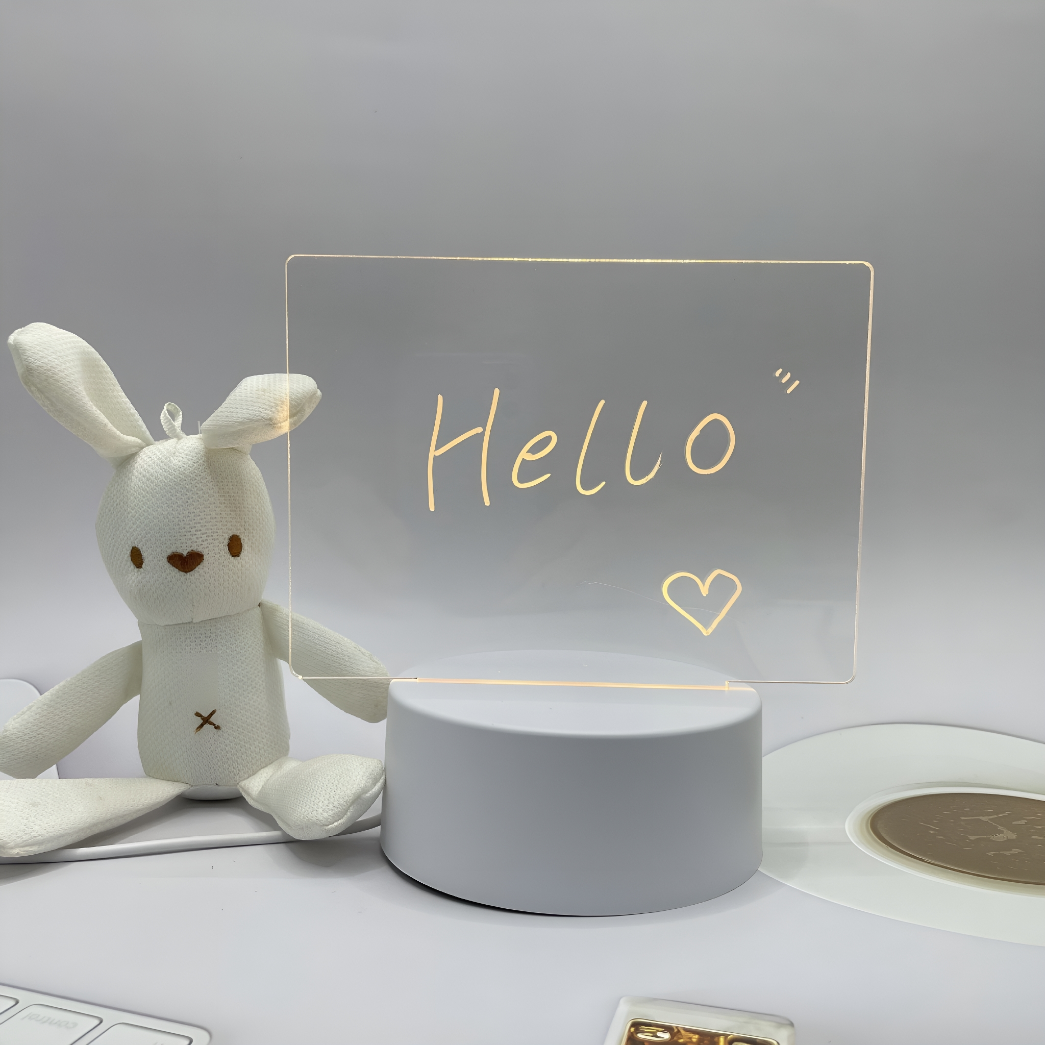 Leuchtschild mit 'Hallo' geschrieben, Hase und Herz. Weißer Hintergrund.