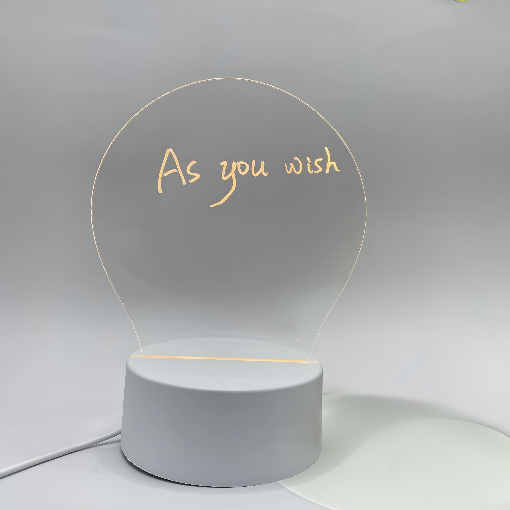 Eine glühbirnenförmige Lampe mit der Aufschrift 'As you wish' auf weißem Sockel.