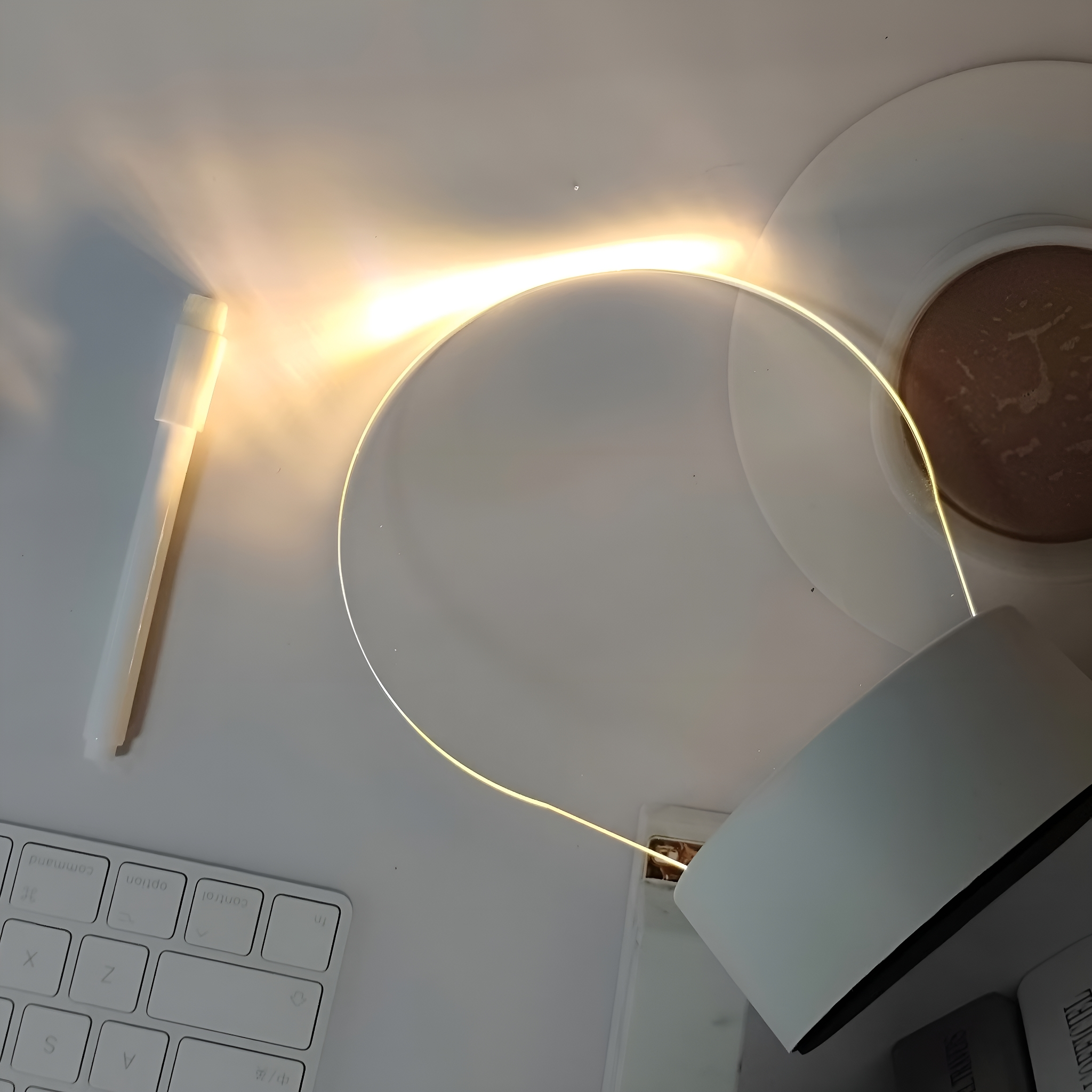 Eine weiße Schreibtischlampe mit ringförmigem Licht steht auf einem Schreibtisch mit Tastatur und Stift.