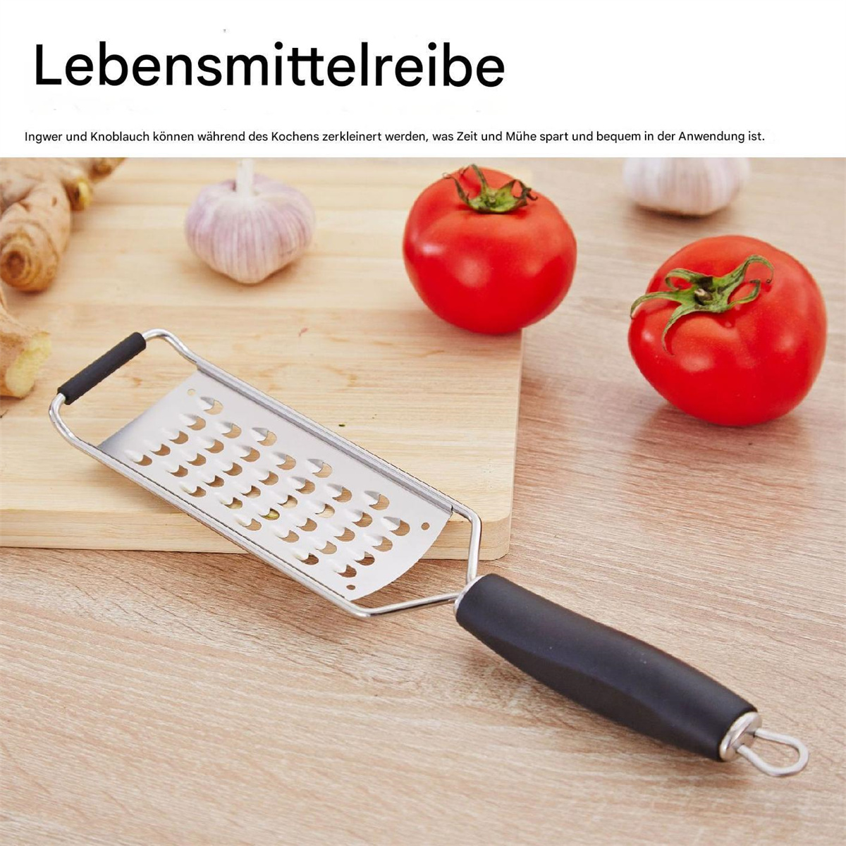 Eine Reibe mit schwarzem Griff und Edelstahl-Reibefläche. Tomaten und Knoblauch auf einem Holzbrett.