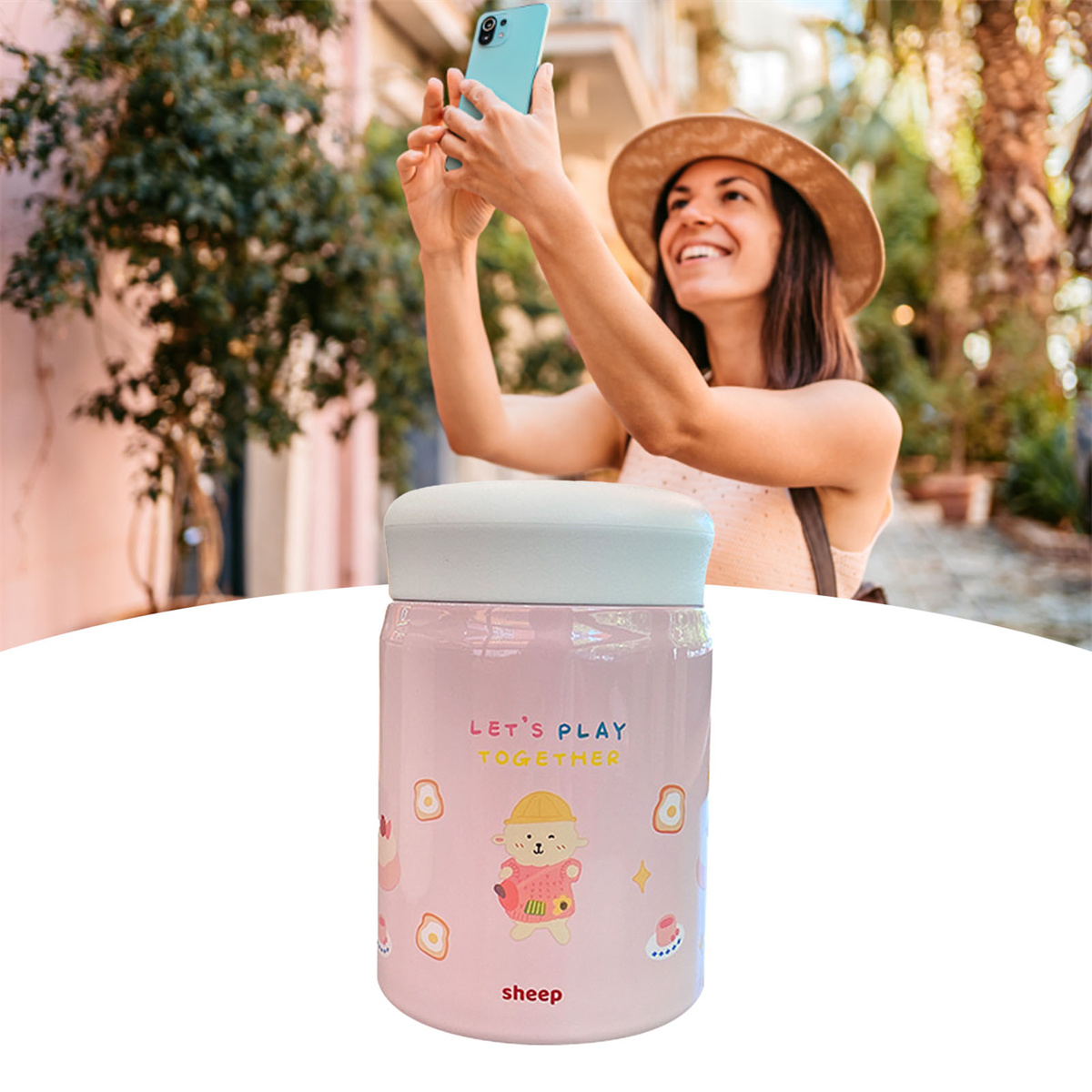Frau macht Selfie mit rosa Tasse. Die Tasse hat ein Schaf-Cartoon und die Worte: "LET'S PLAY TOGETHER".