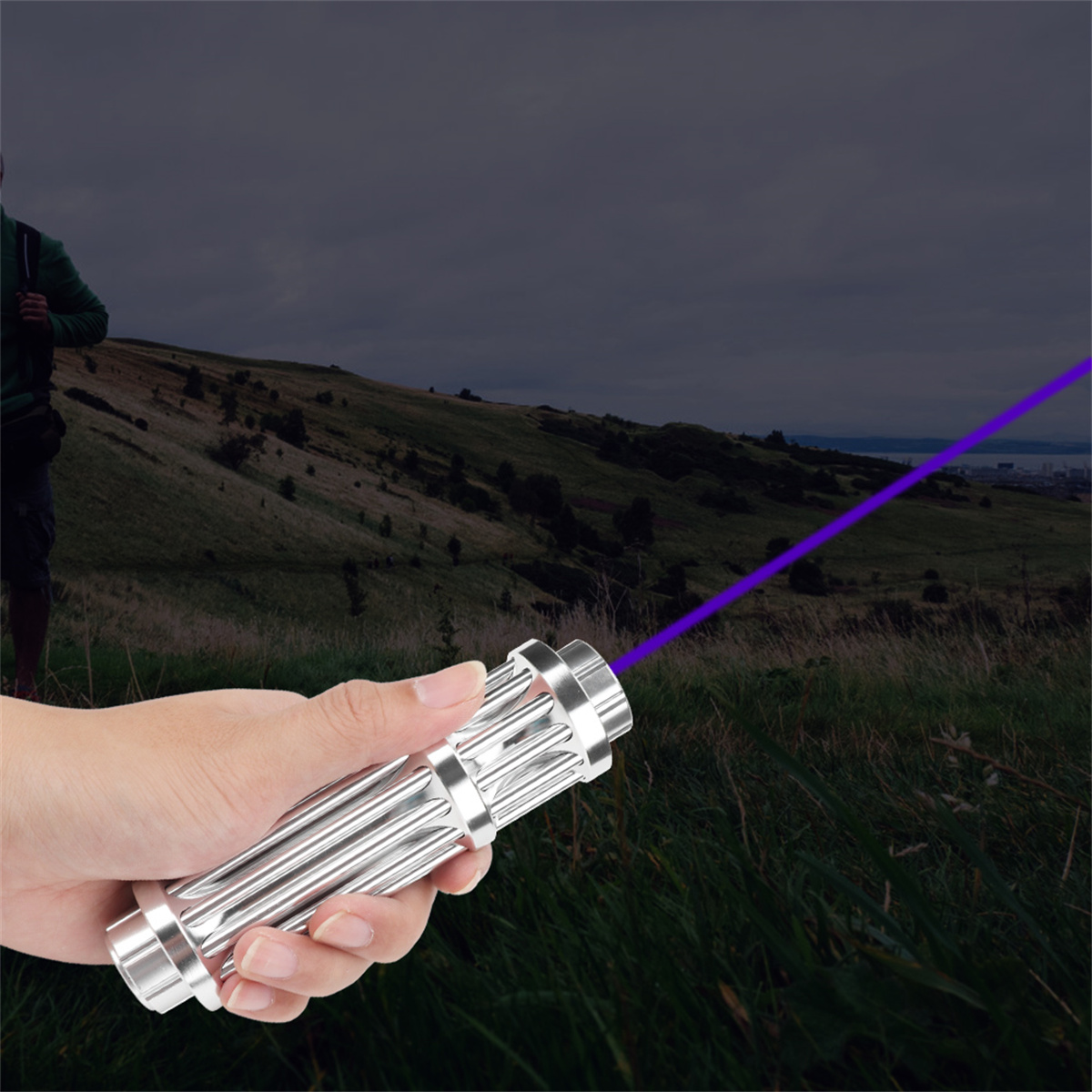 Eine Hand, die einen silbernen Laserpointer hält, der einen lila Strahl in einem Feld aussendet.