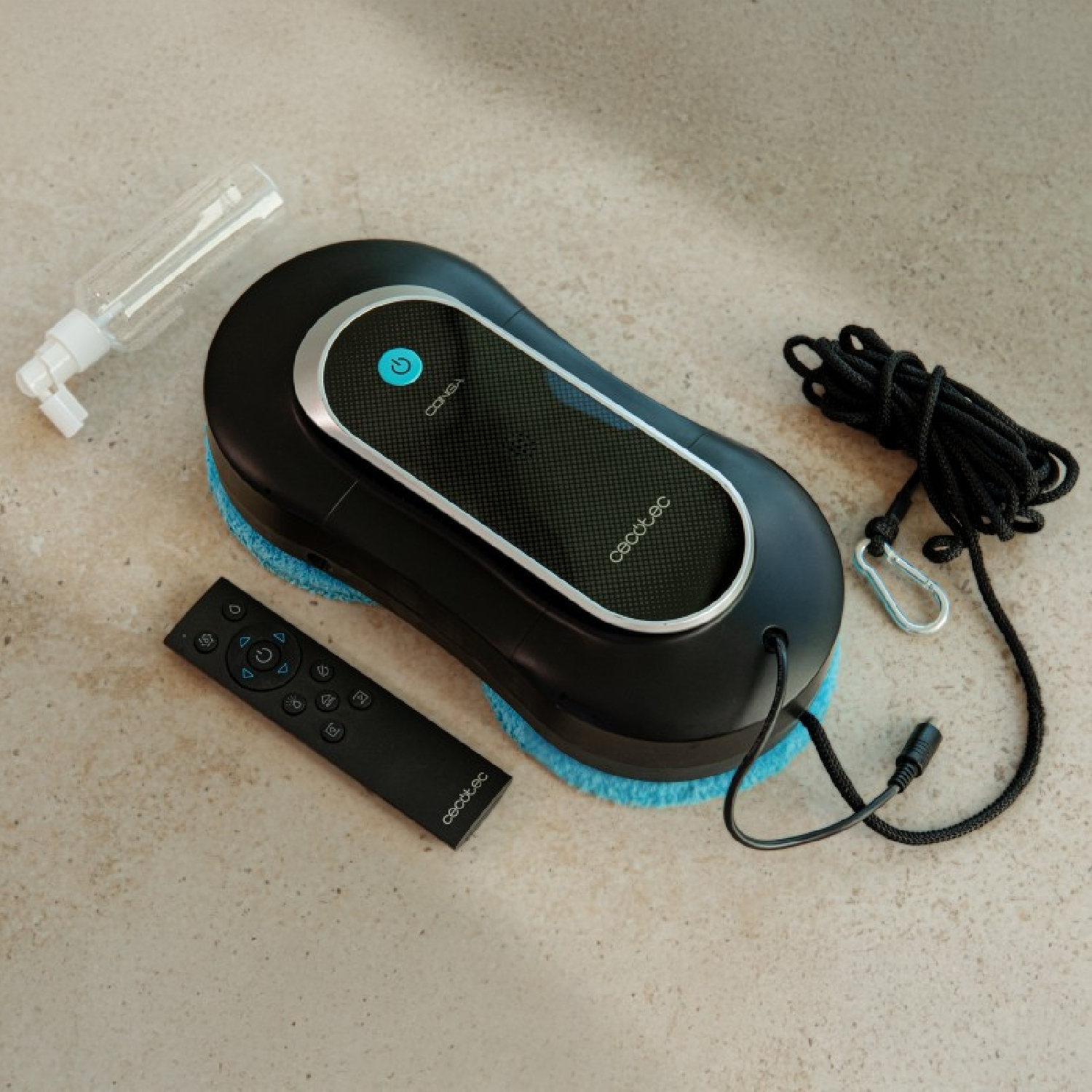 Schwarzer Fensterputzroboter mit Zubehör auf beiger Oberfläche. Inklusive Sprühflasche und Fernbedienung.