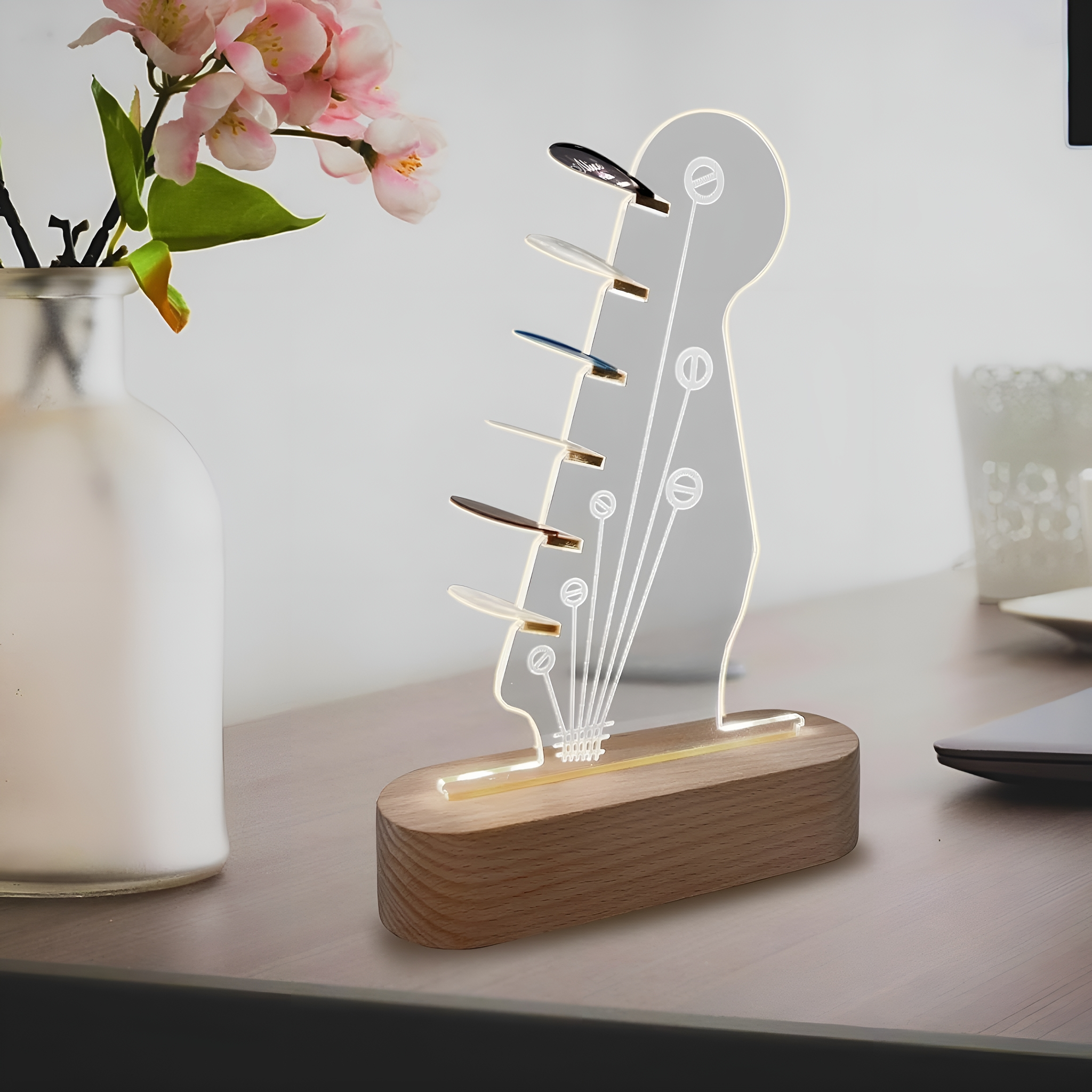 Gitarrenkopf-förmige Lampe auf Holzsockel. Mit Plektren und einer Vase mit Blumen daneben.