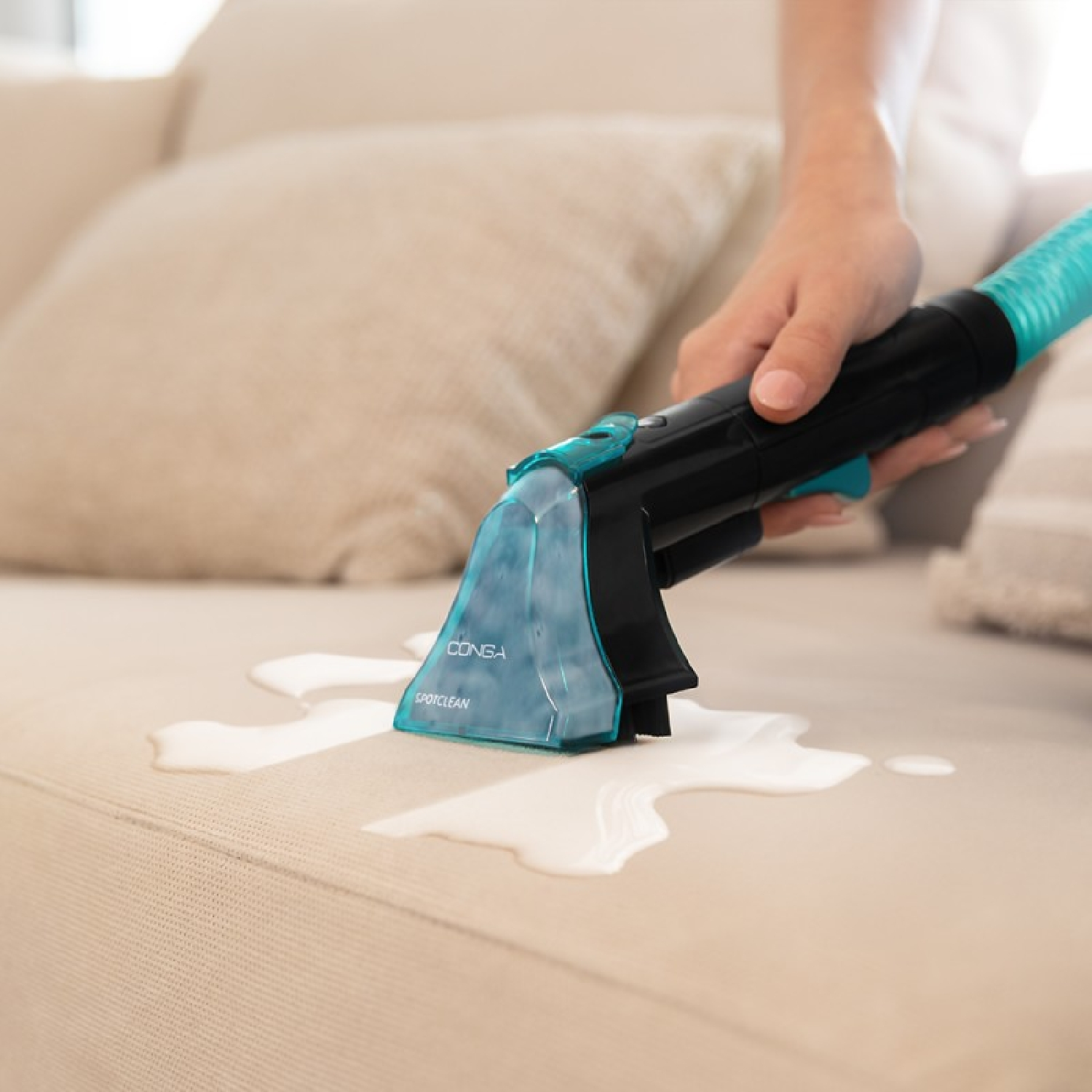 Mano che pulisce un divano bianco con uno smacchiatore, lasciando una macchia d'acqua.