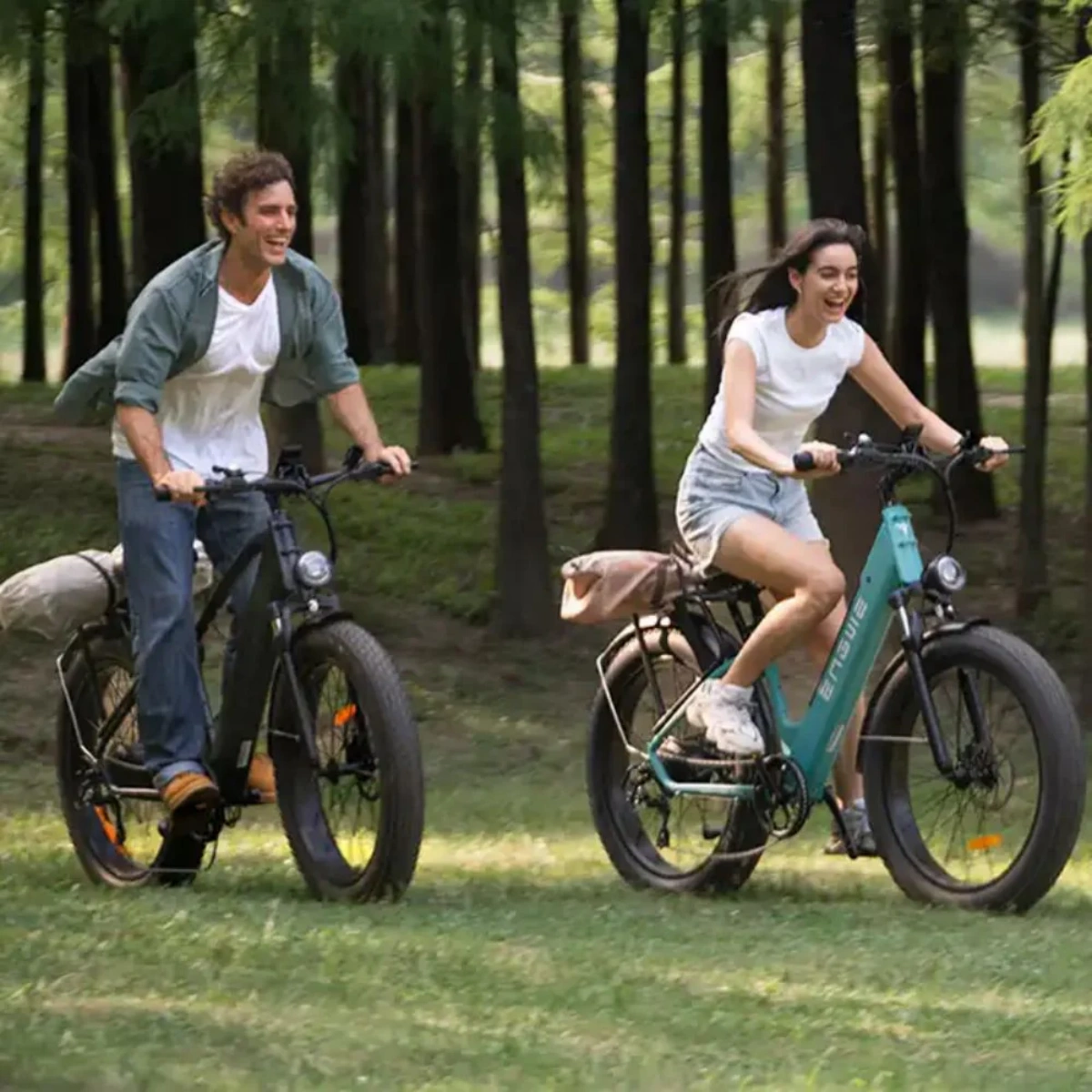 Due persone che vanno in e-bike in un parco. Biciclette verdi, alberi ed erba. Giornata di sole.