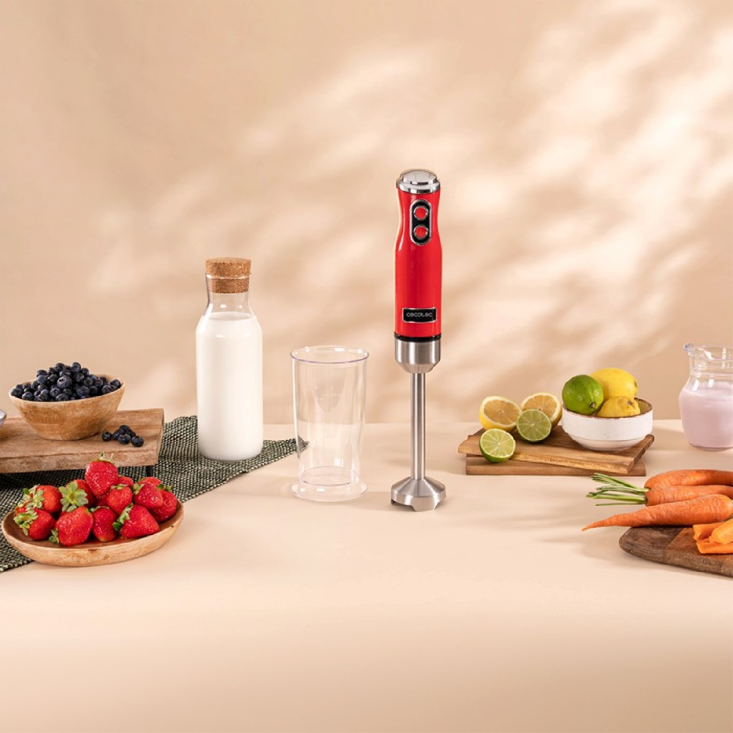 Un frullatore a immersione rosso con ingredienti su un tavolo: fragole, limoni, latte.