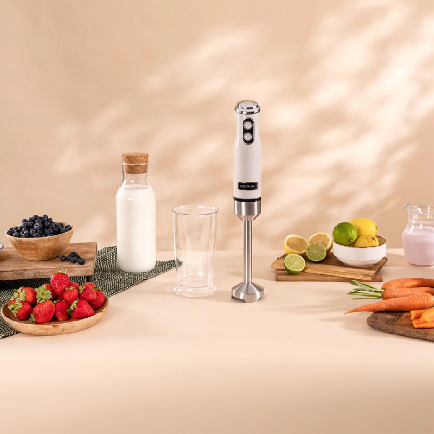 Frullatore, latte, bicchiere, fragole, mirtilli, limoni, lime, carote su un tavolo, sfondo beige.