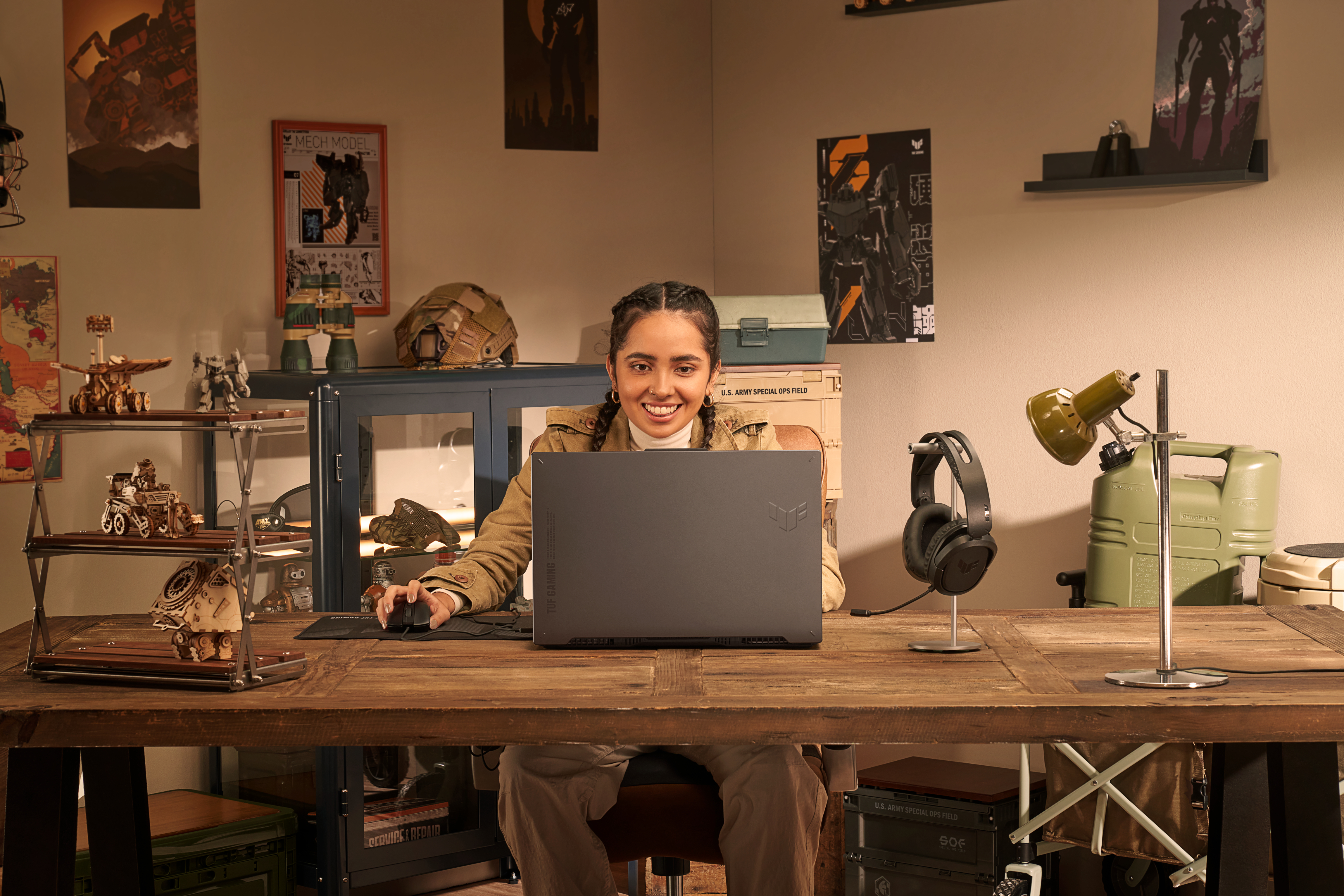 Frau lächelt an einem Laptop auf einem Schreibtisch. Der Schreibtisch hat verschiedene Gegenstände. Kopfhörer und Monitor.