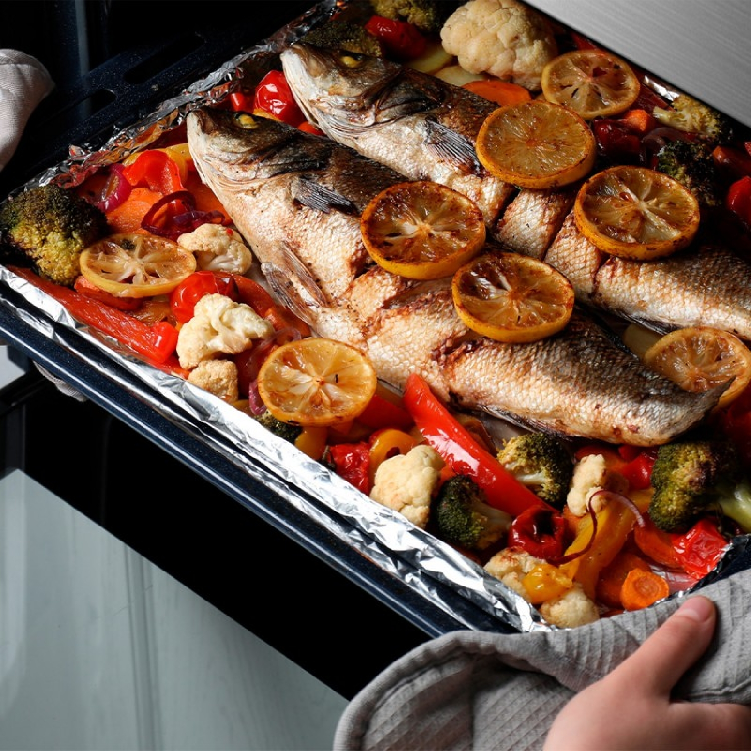 Backblech mit gebackenem Fisch, Zitronenscheiben und Gemüse.