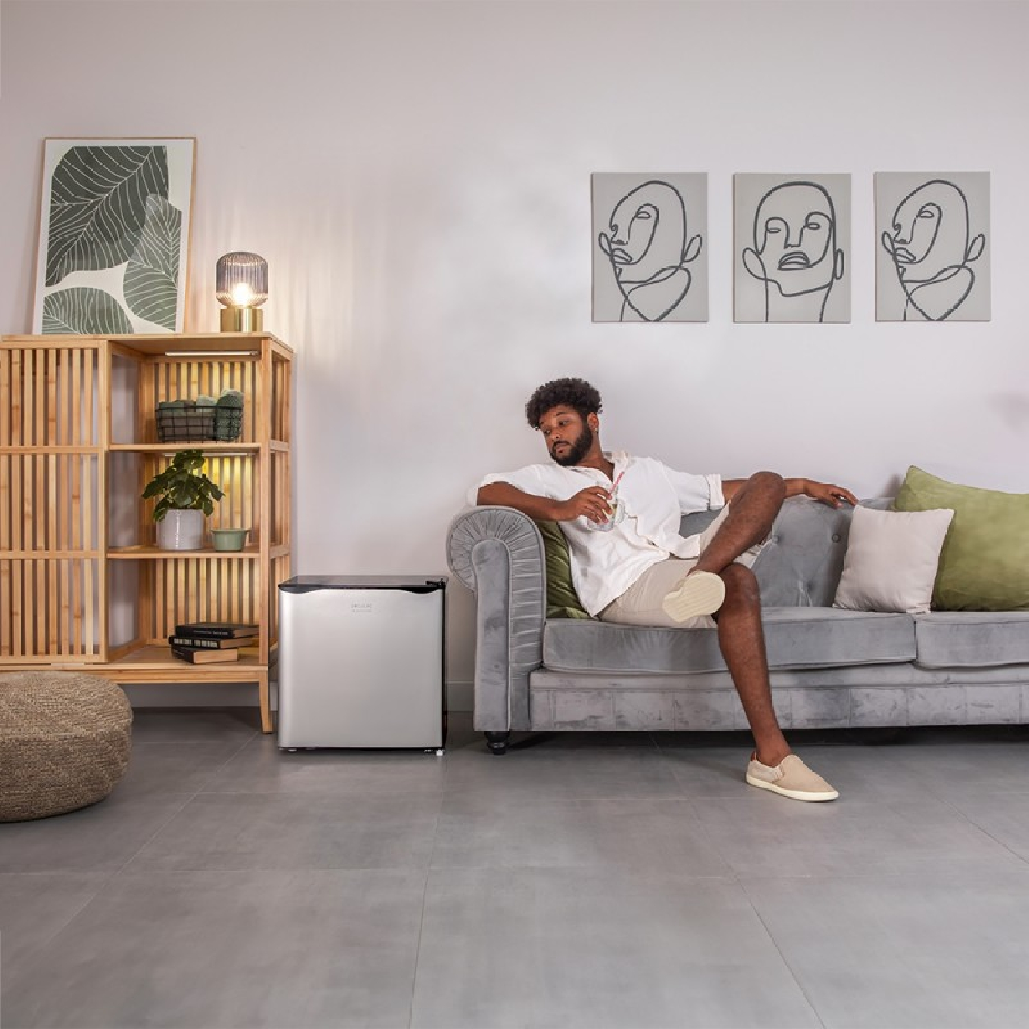 Mężczyzna siedzi na szarej kanapie ze stolikiem i lodówką w salonie.