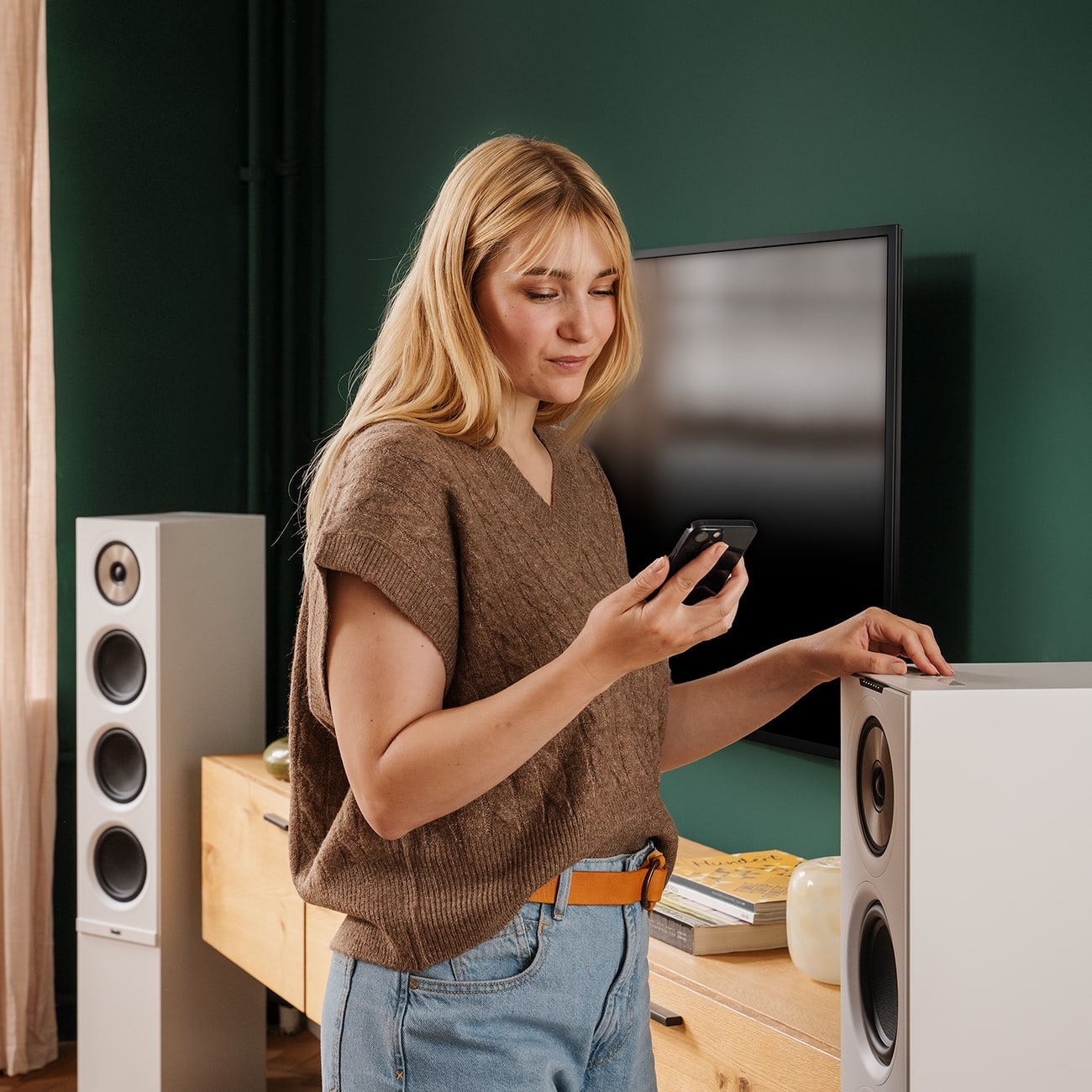 Eine Frau benutzt ein Telefon in der Nähe von Lautsprechern und einem Holzschrank in einem modernen Wohnzimmer.