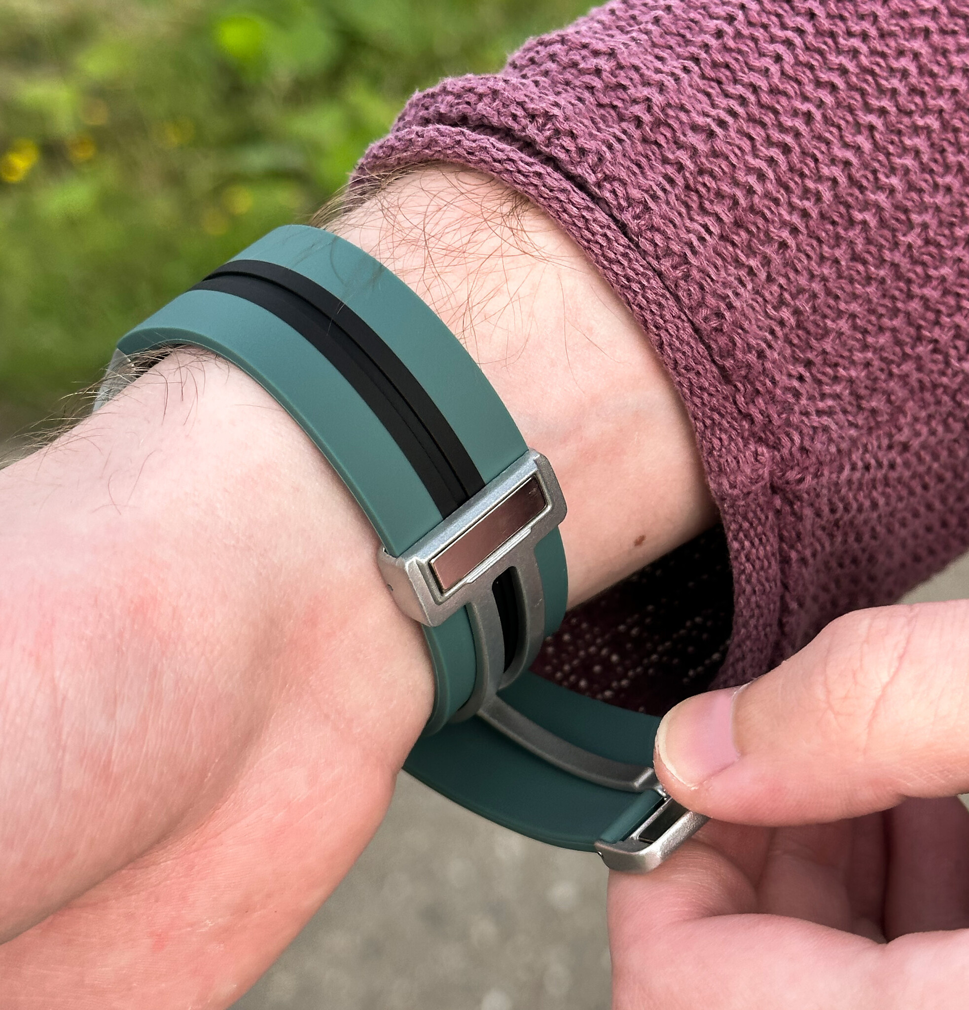 Person trägt ein tealfarbenes Uhrenarmband mit schwarzen Streifen, das am Handgelenk befestigt wird.