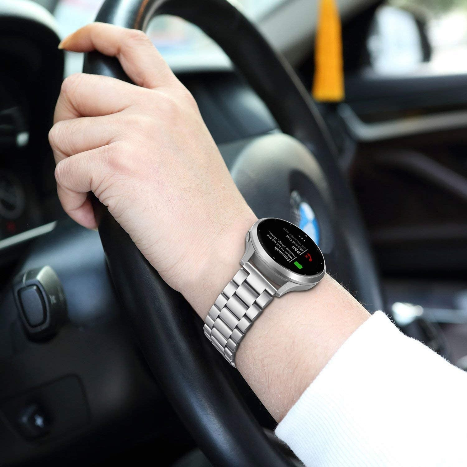 Eine Person, die eine silberne Uhr am Handgelenk trägt, während sie ein Lenkrad hält.