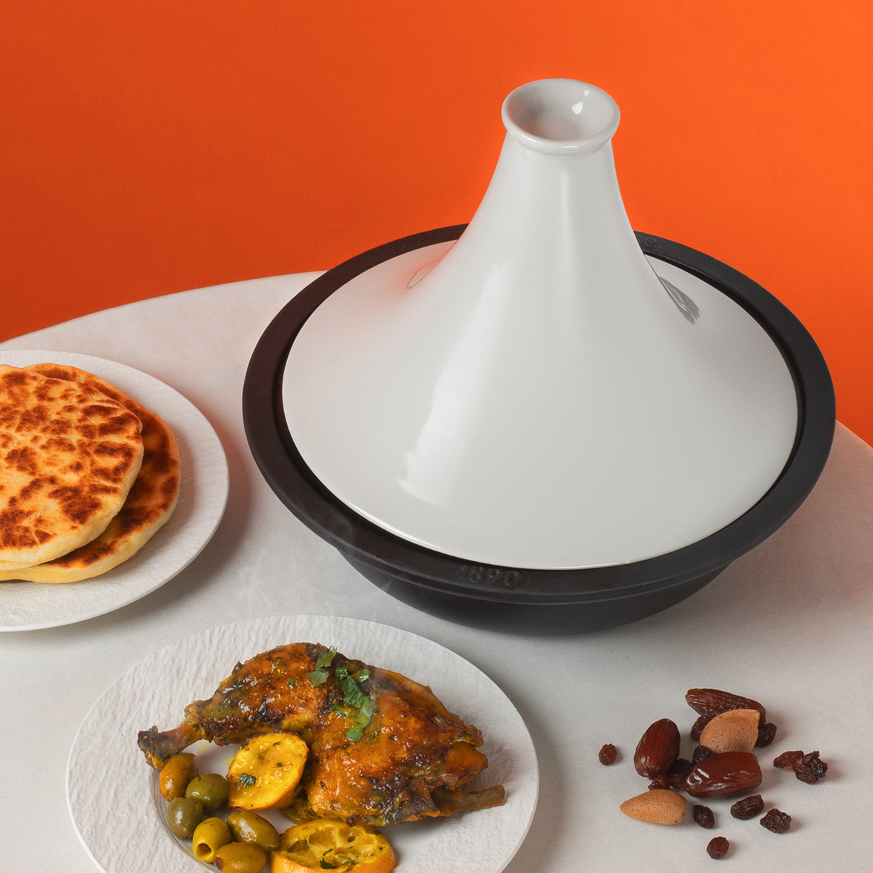 Un piatto tagine bianco e nero con cibo cotto su un tavolo con piatti di cibo.