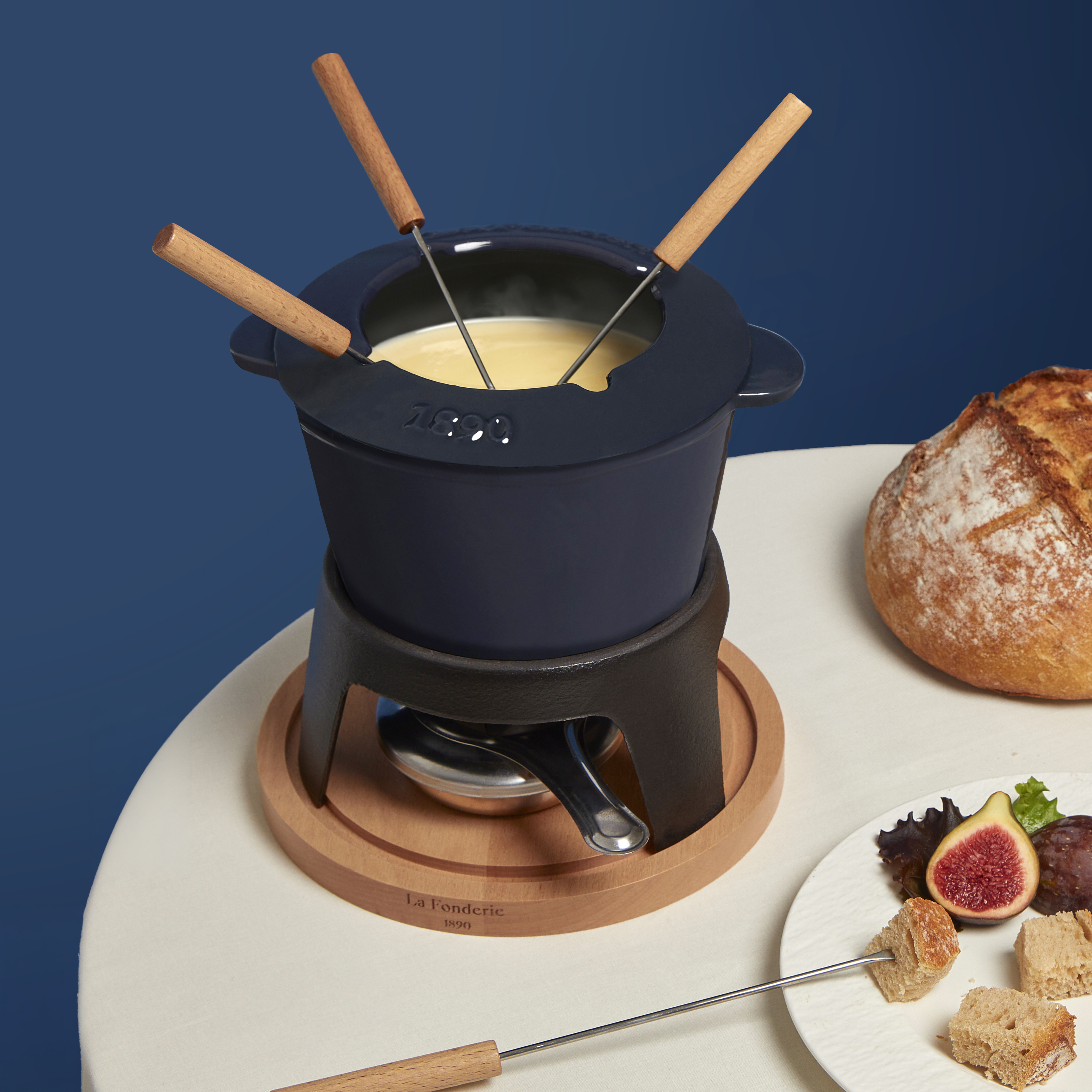 Fondue-Set auf einem weißen Tisch. Es enthält einen Topf mit Holzgriffen, Brot und Essen auf einem Teller.