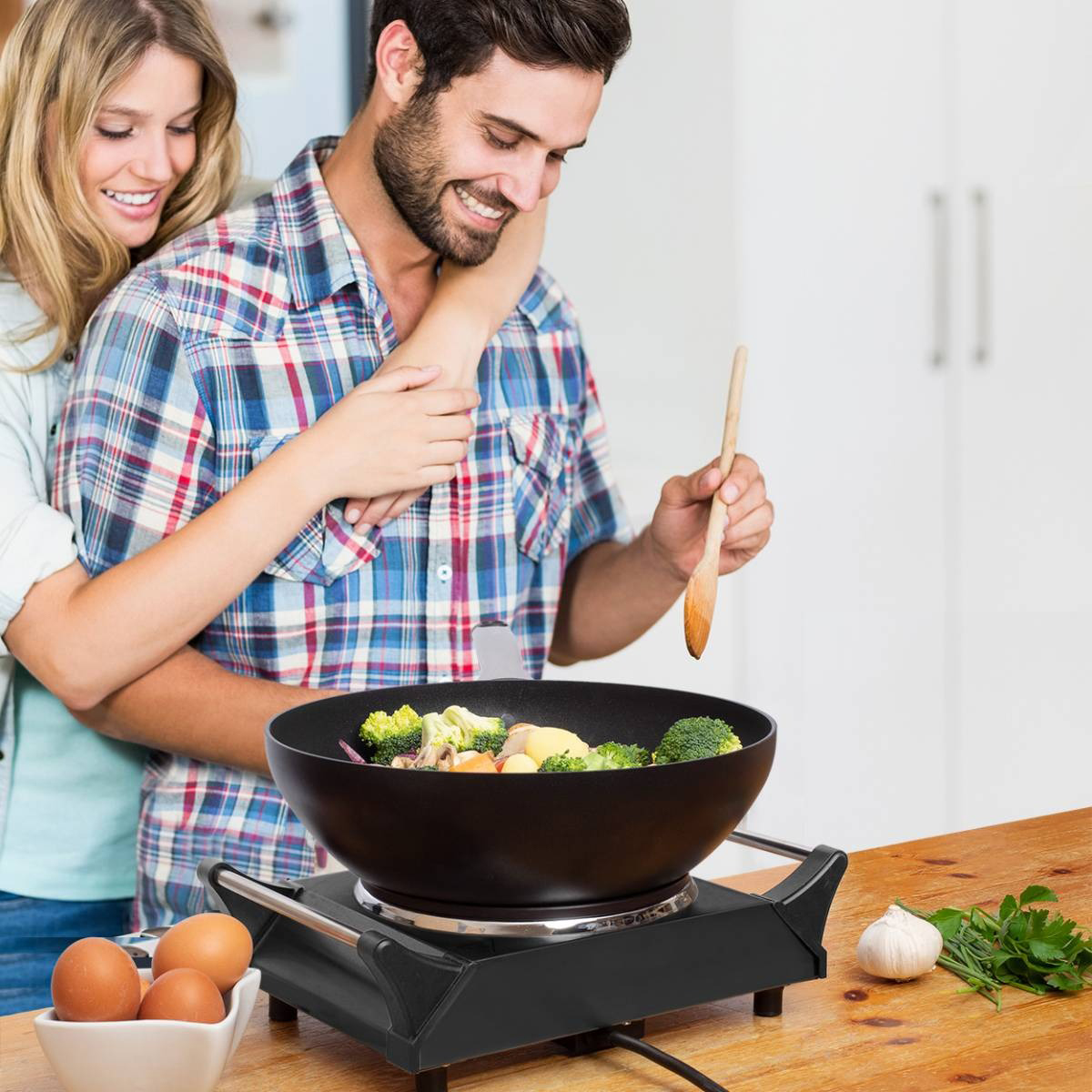 Couple cuisinant, homme remuant des légumes dans un wok sur une plaque portable.