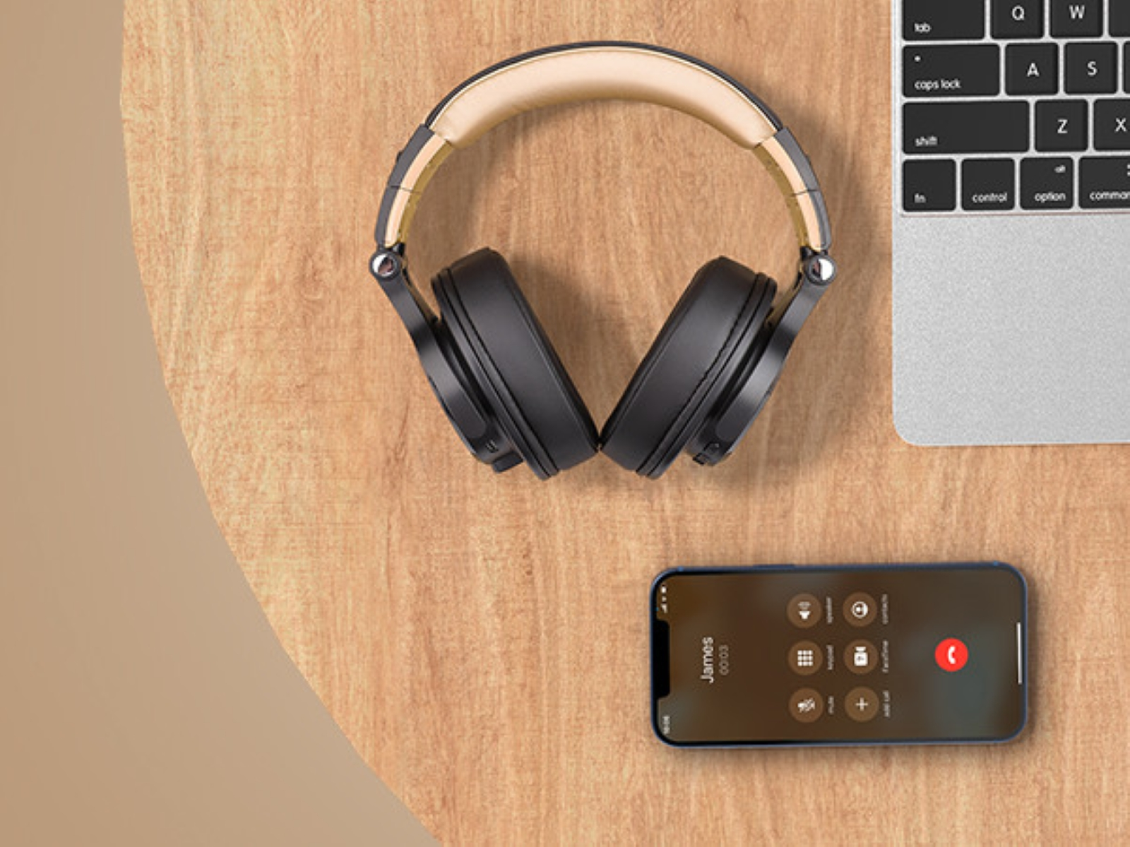Headphones on a wooden table, with a phone and a laptop. Phone is on call.